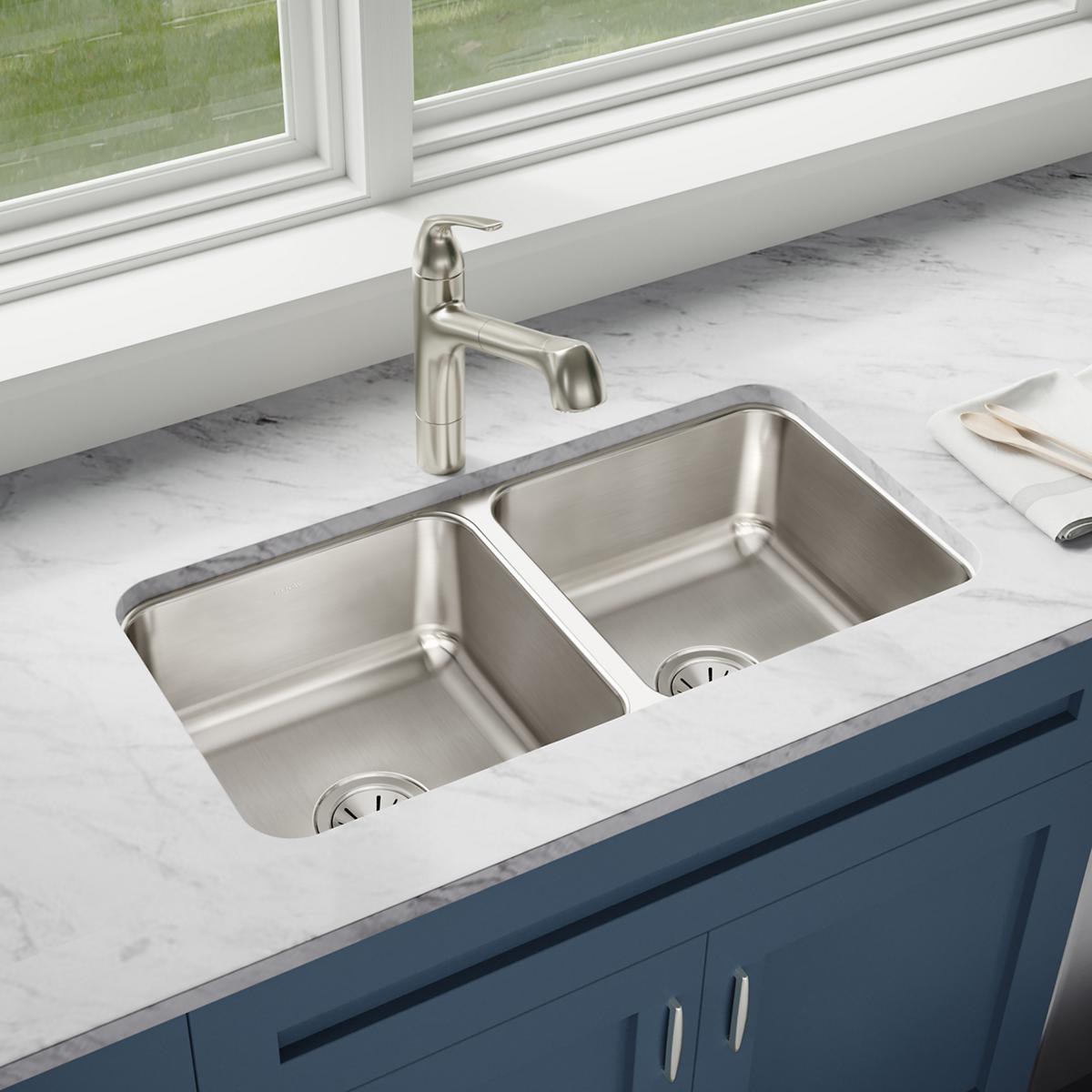 Stainless steel double bowl undermount sink installed in white marble countertop with nickel faucet.