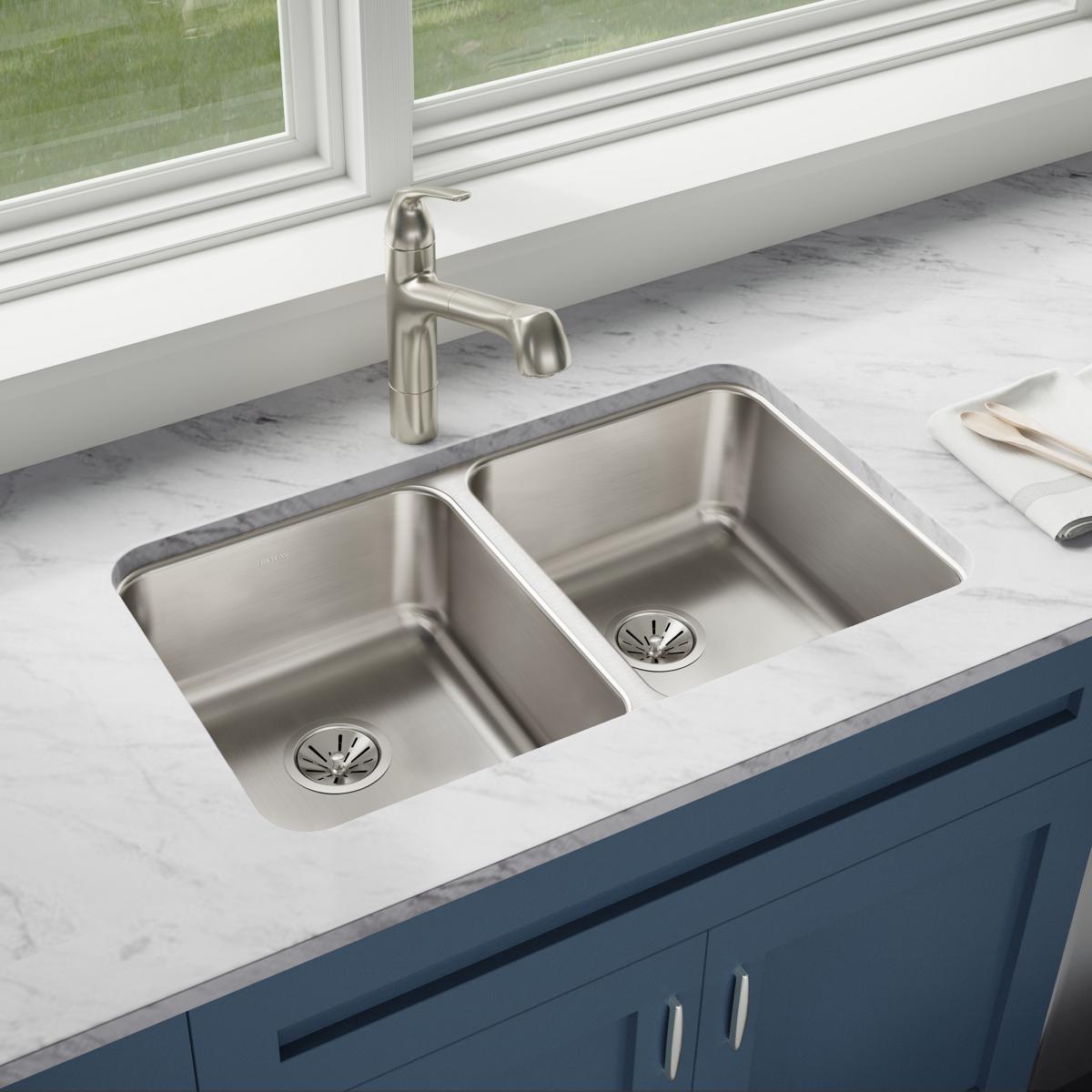 Stainless steel double bowl undermount sink installed in white marble countertop with matching faucet and drain strainers.