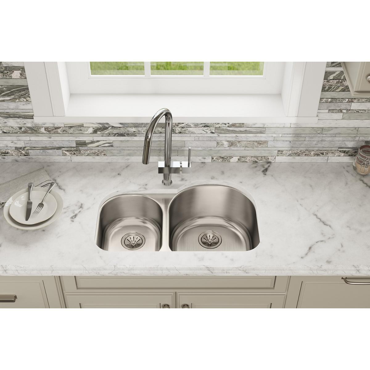 Stainless steel double bowl undermount sink with offset bowls installed in white marble countertop beneath chrome faucet and 