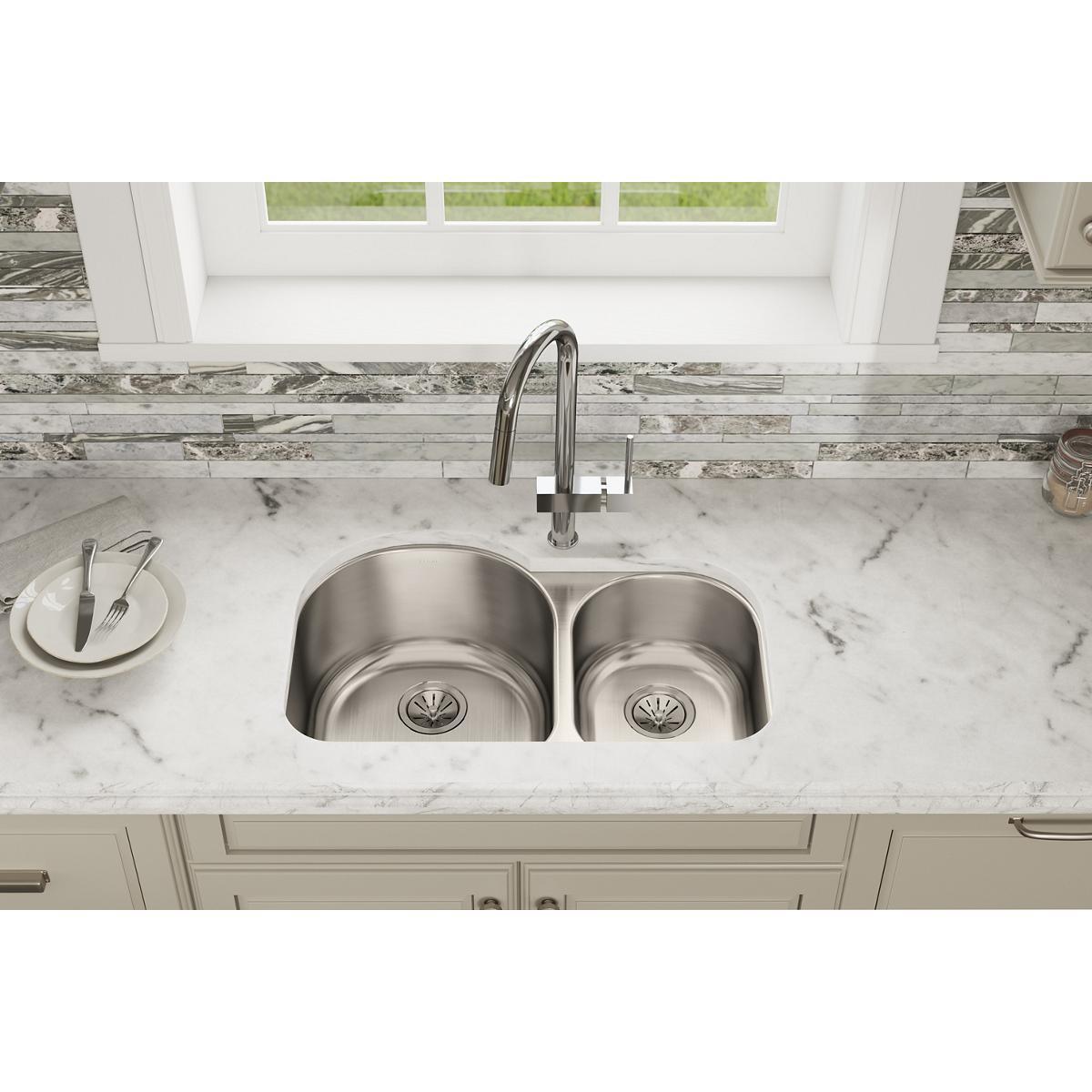 Stainless steel undermount sink with two bowls of different sizes installed in a marble countertop with faucet.