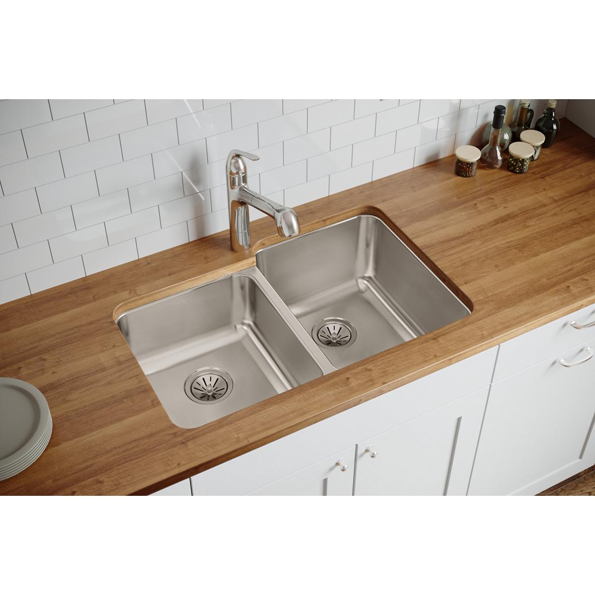 Stainless steel double bowl undermount sink with offset bowls installed in wood countertop beneath white subway tile backspla