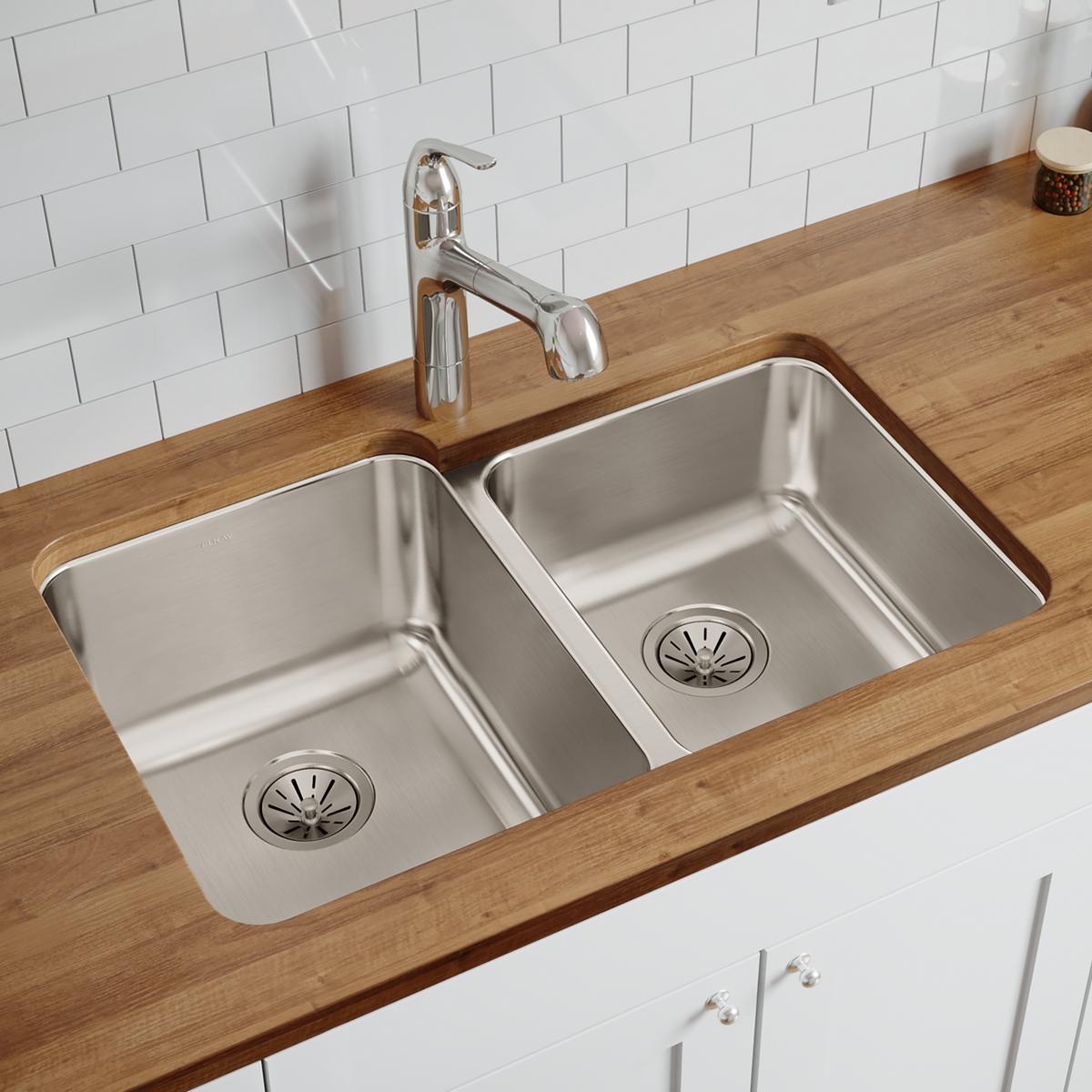 Stainless steel double bowl undermount sink installed in wood countertop with chrome faucet and white subway tile backsplash.