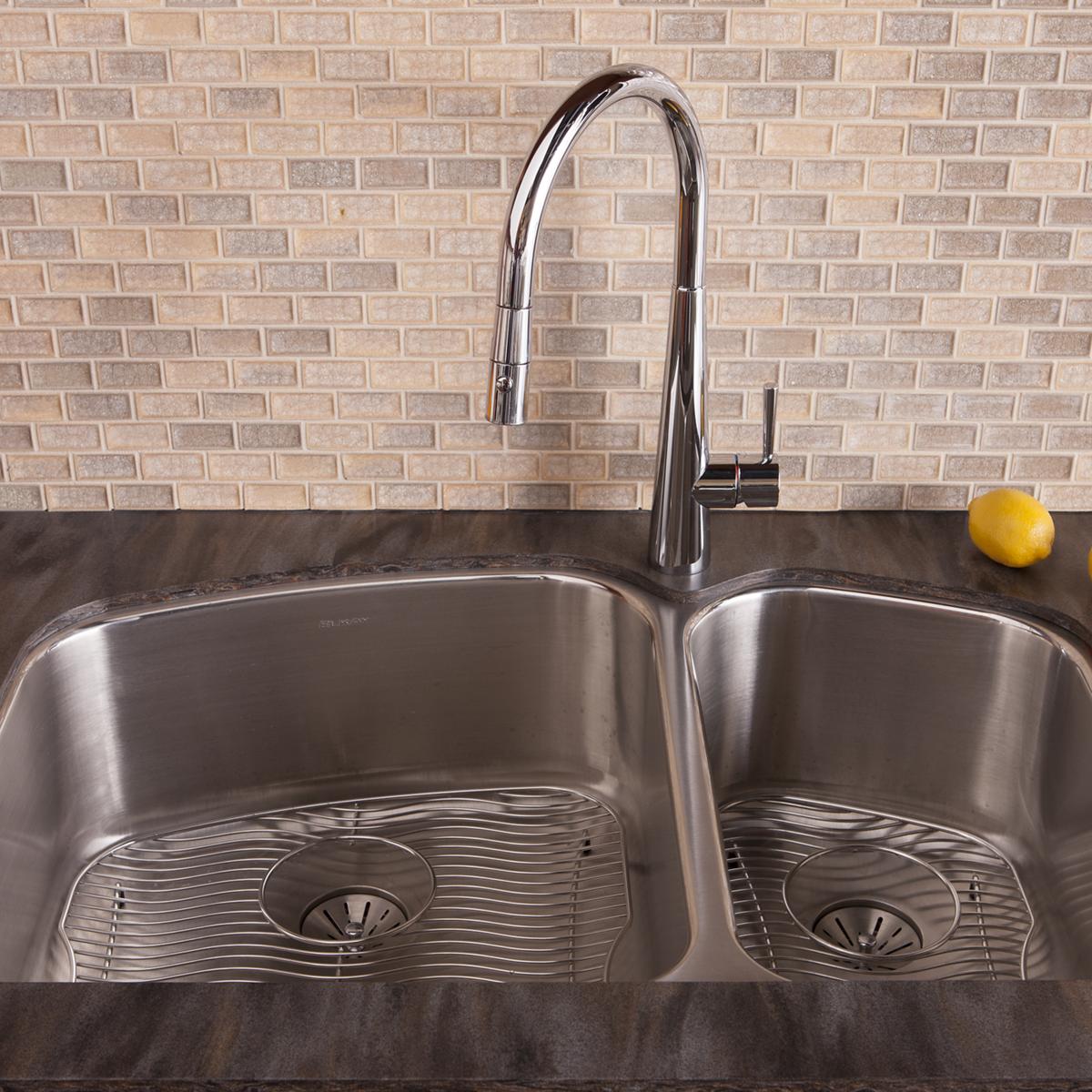 Stainless steel double bowl undermount sink with two drain baskets installed in dark countertop, paired with chrome pull-down