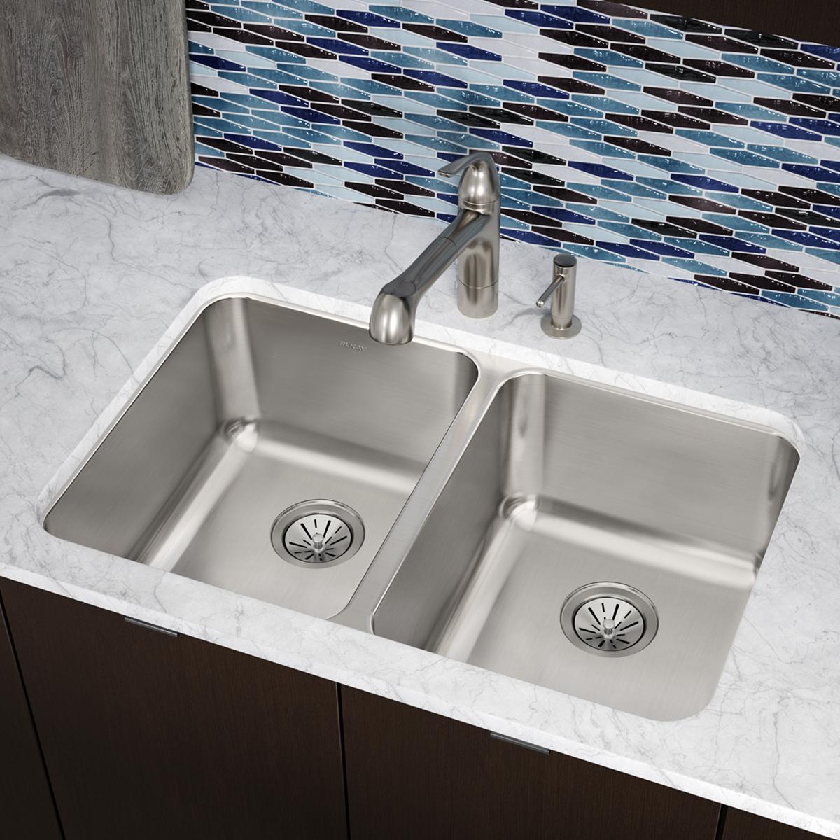 Stainless steel double bowl undermount sink installed in marble countertop with faucet and blue tile backsplash.