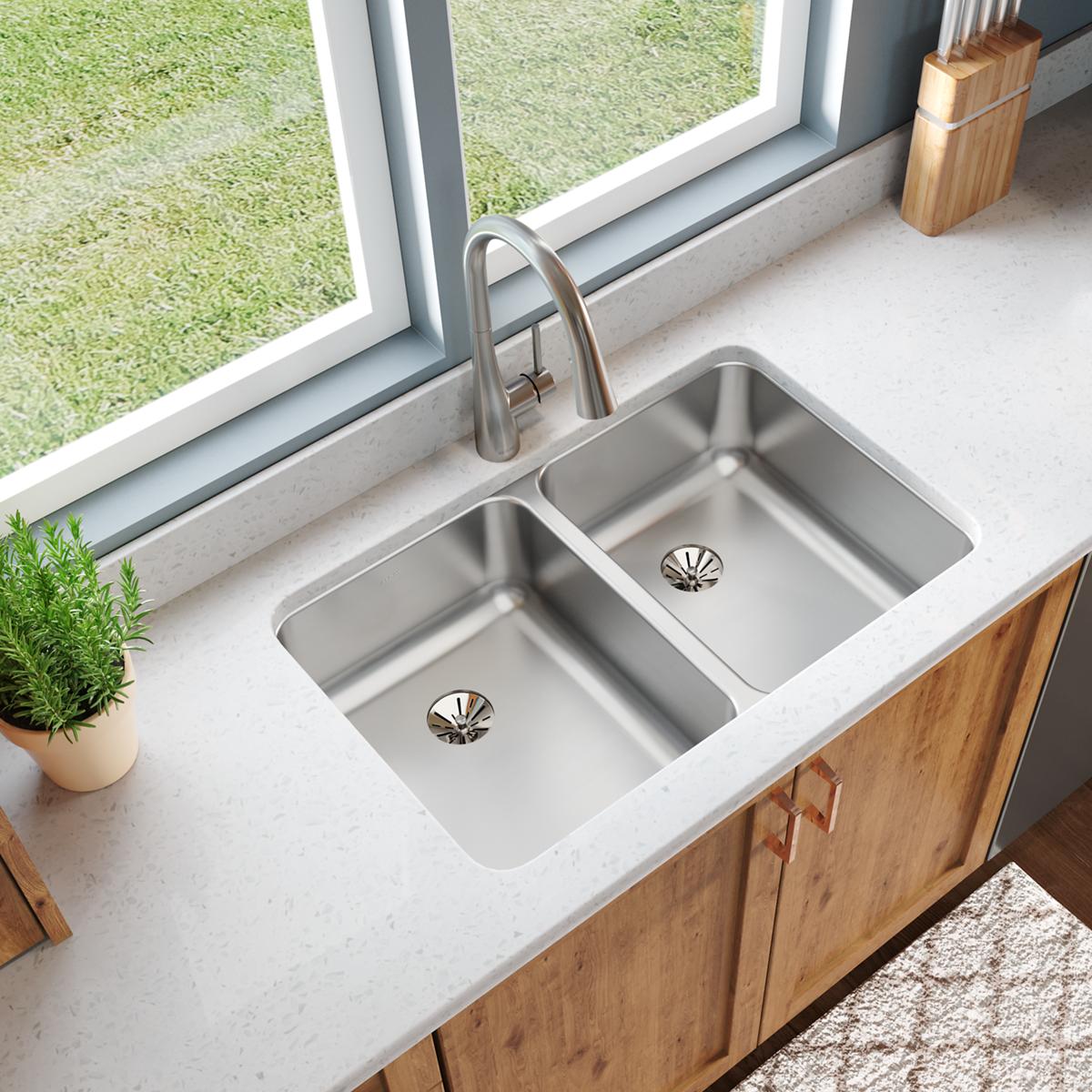 Stainless steel double bowl undermount sink installed in white countertop with curved faucet and two drain strainers visible.
