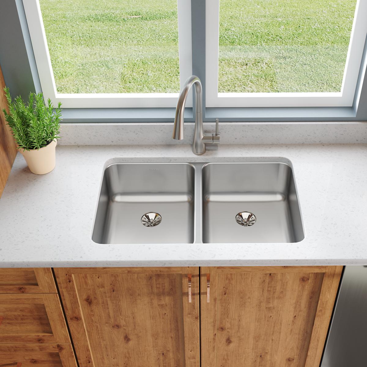 Stainless steel double bowl undermount sink with two drain openings installed in light countertop above wood cabinetry.