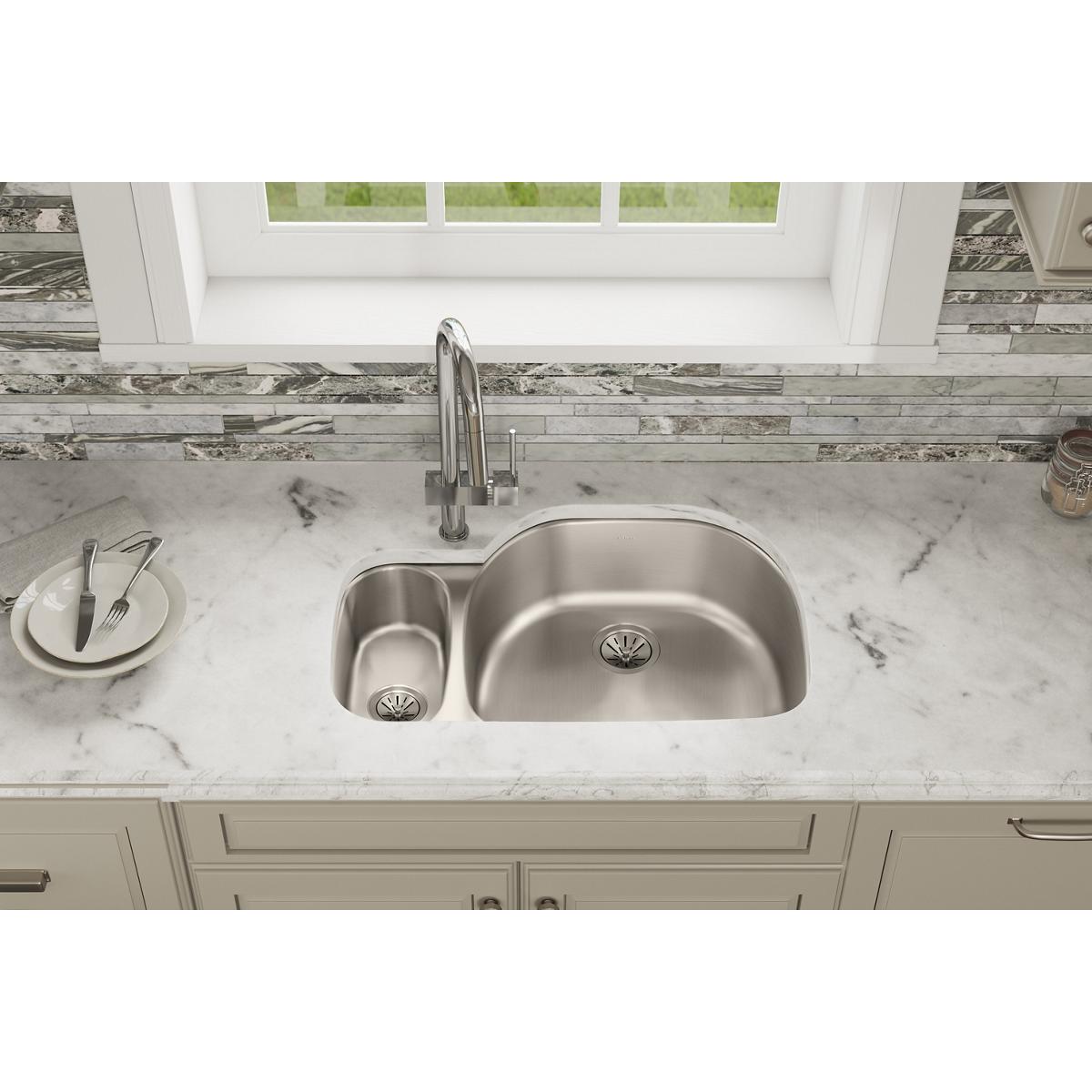 Stainless steel double bowl undermount sink with one smaller and one larger basin installed in marble countertop.