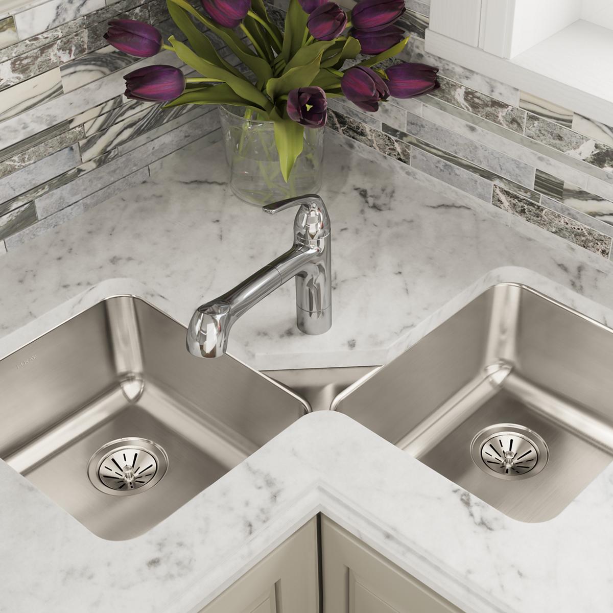 Stainless steel double bowl corner sink with chrome faucet installed in marble countertop.