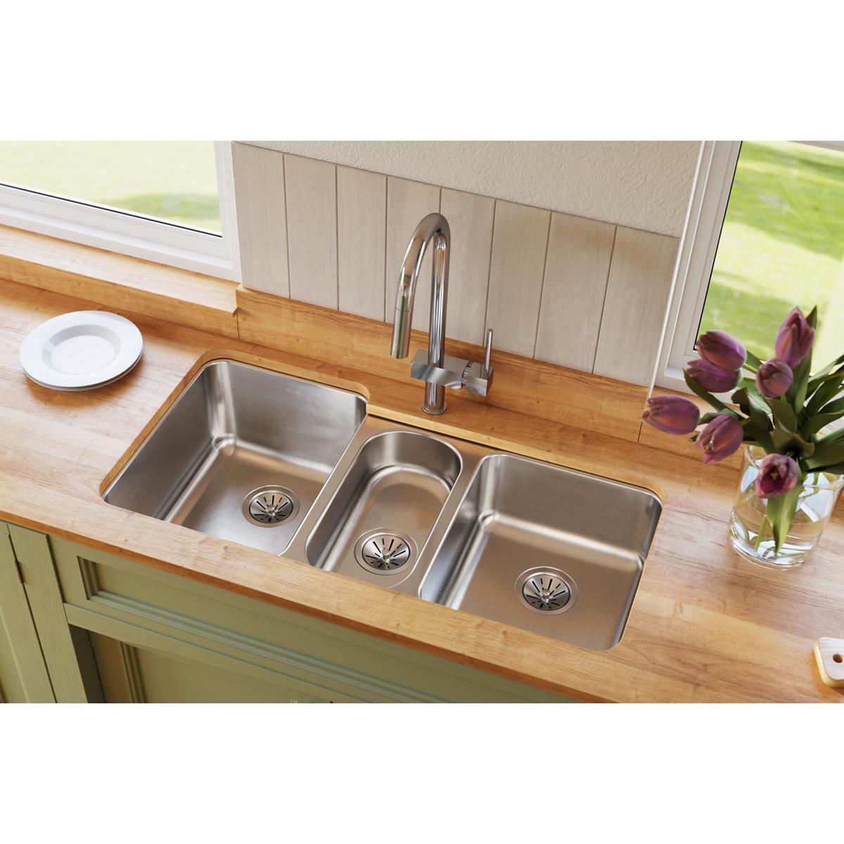 Stainless steel triple bowl undermount sink installed in wooden countertop with chrome faucet and drain strainers.