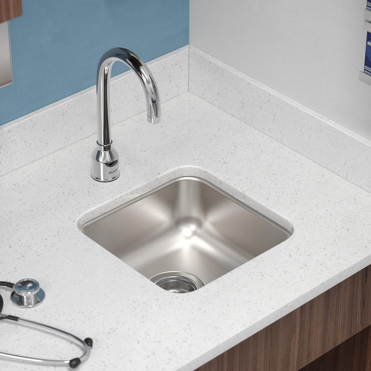 Stainless steel square undermount sink with single bowl installed in white countertop with chrome faucet.