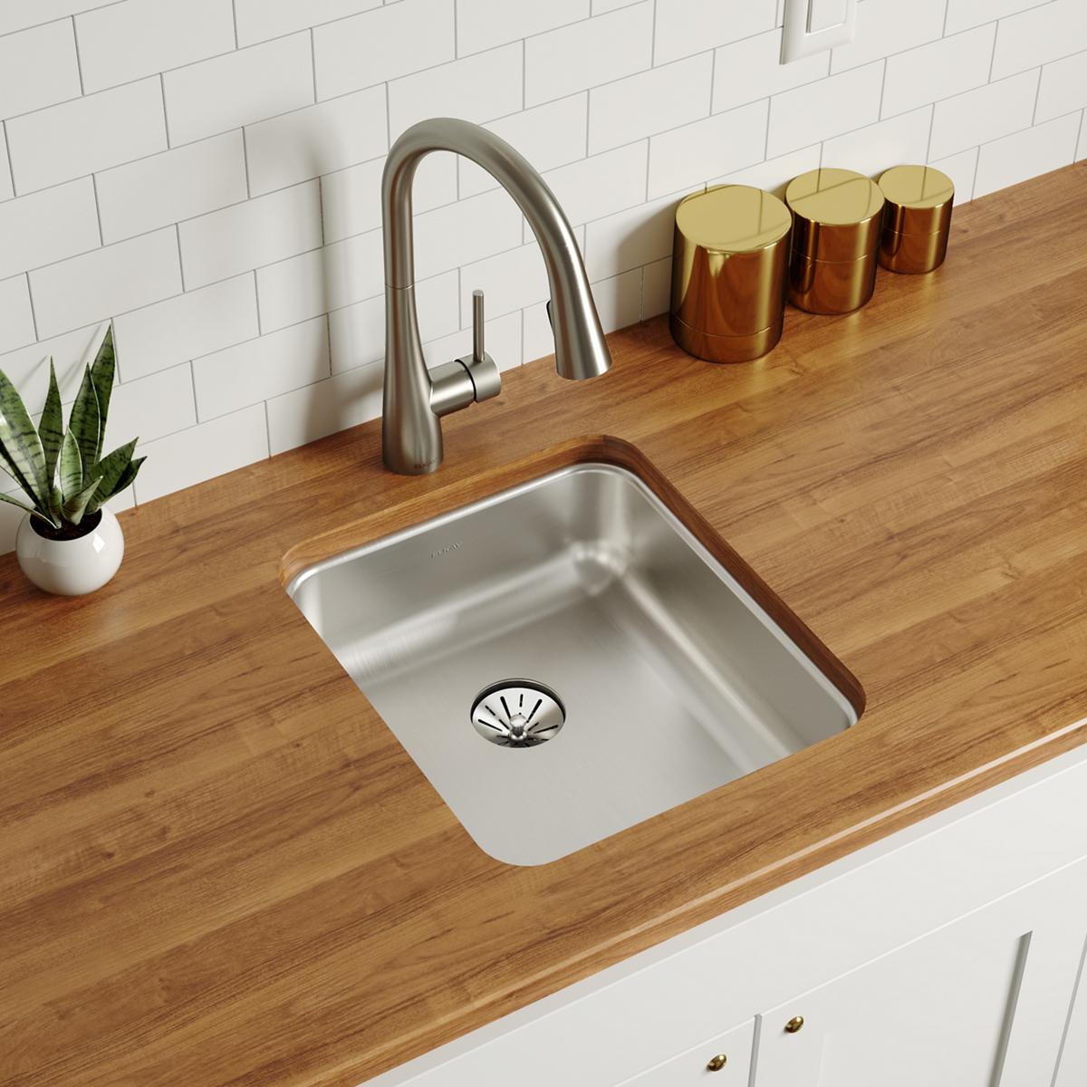 Stainless steel single bowl undermount sink installed in wood countertop with arched faucet and drain strainer visible.