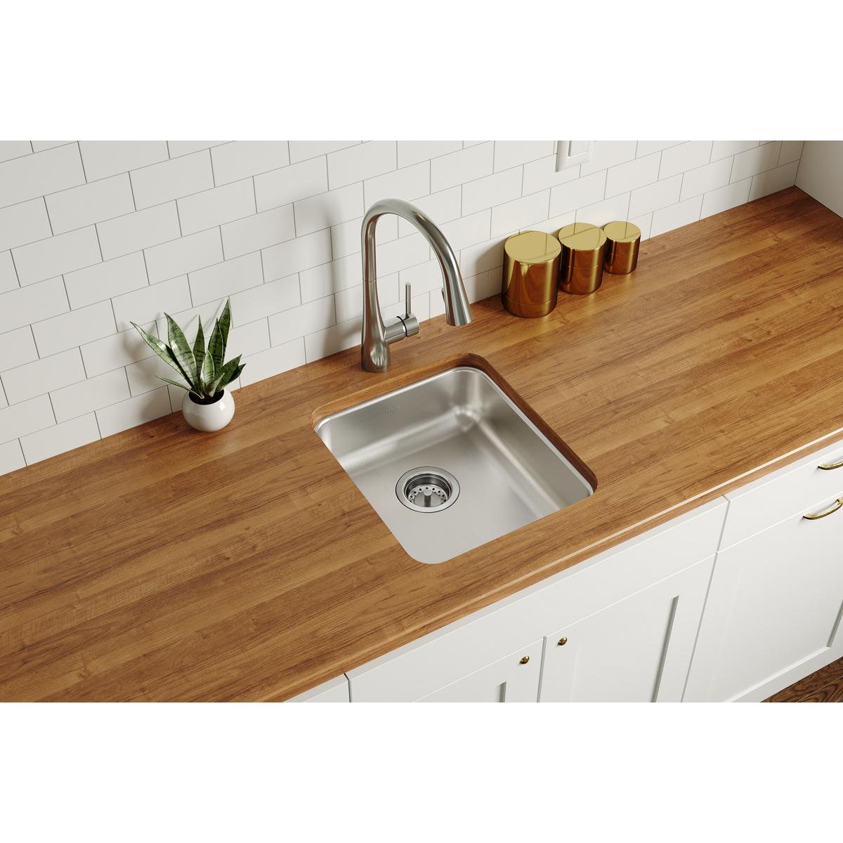 Stainless steel single bowl undermount sink installed in wood countertop with faucet and drain strainer visible.