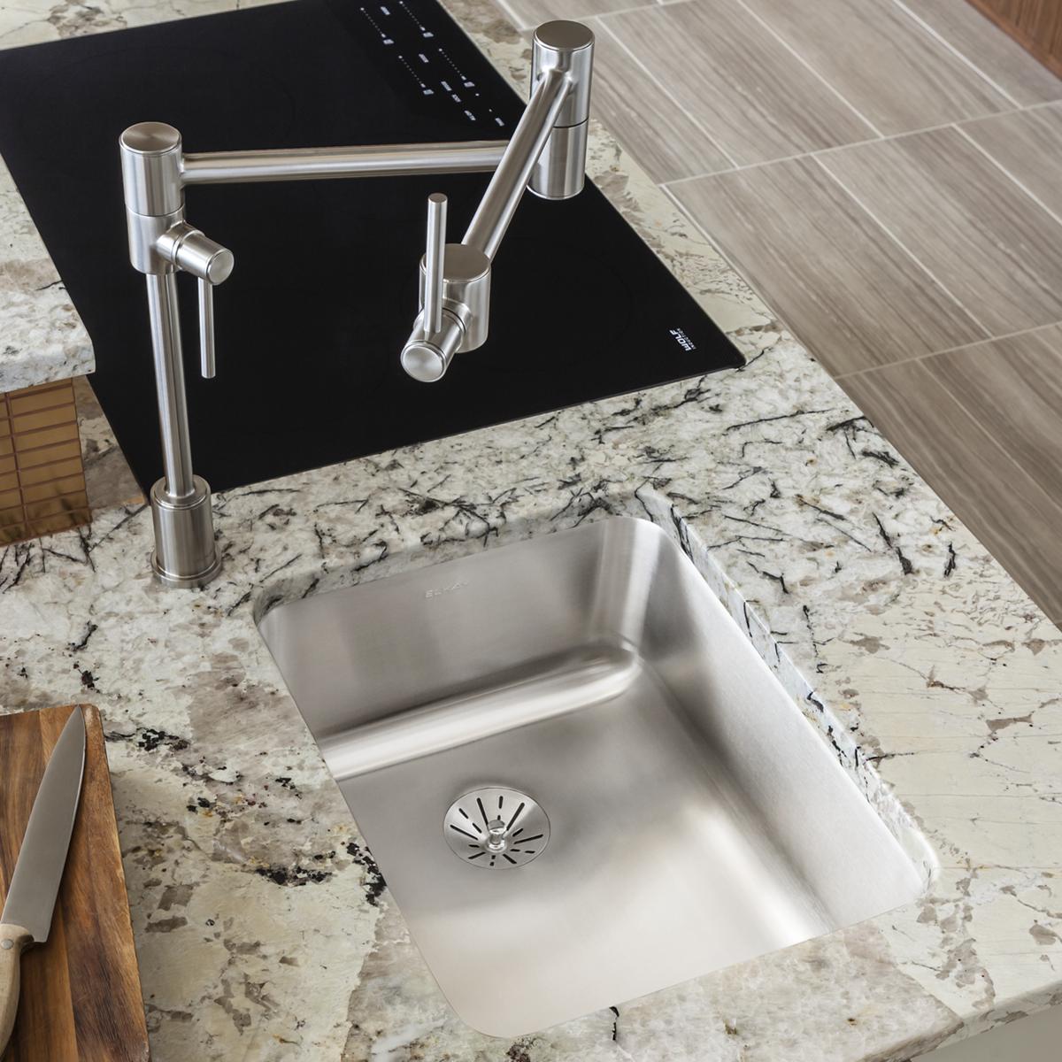 Stainless steel single-bowl undermount sink installed in granite countertop with chrome faucet and drain strainer visible.