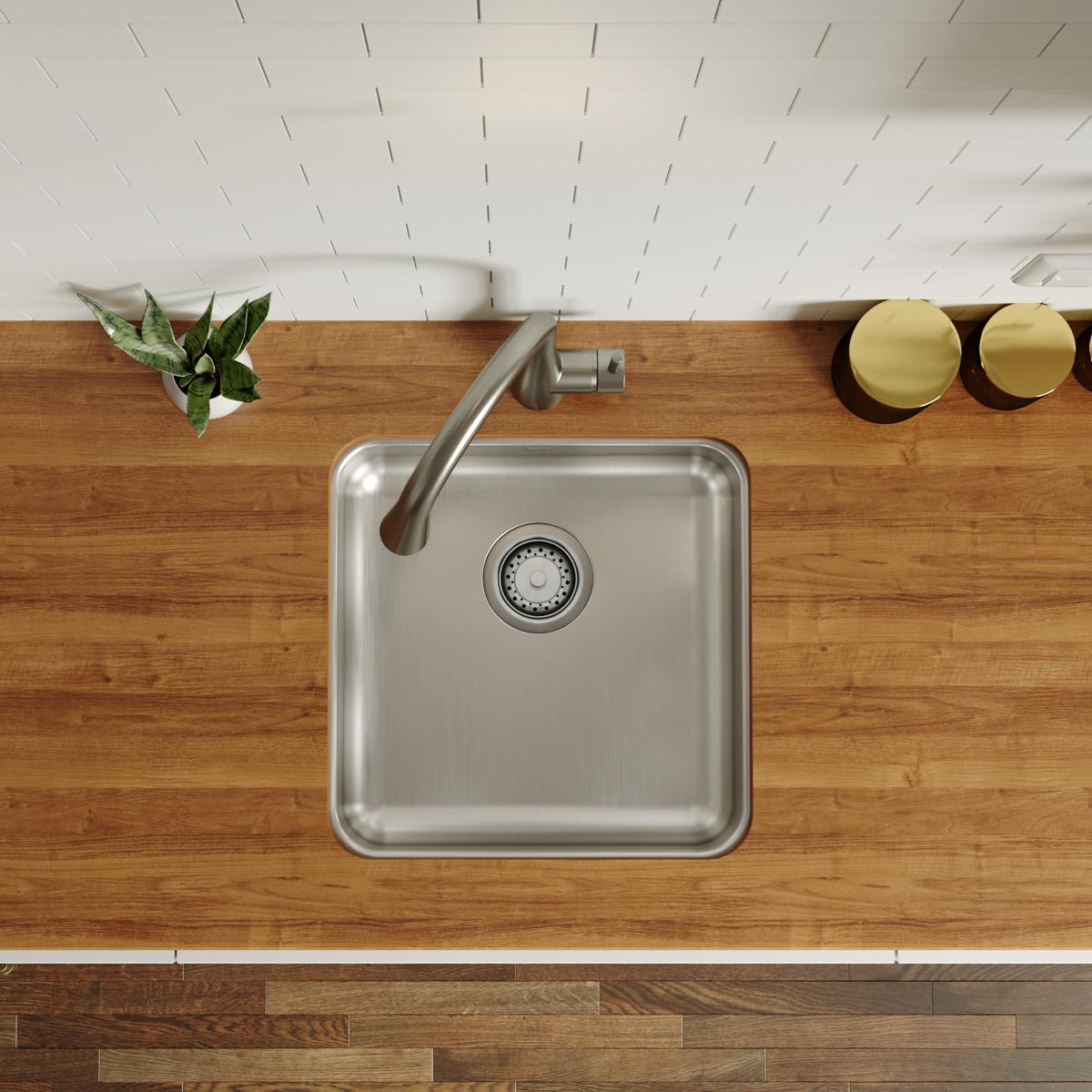 Square stainless steel undermount sink with single bowl and drain strainer, installed beneath wood countertop.