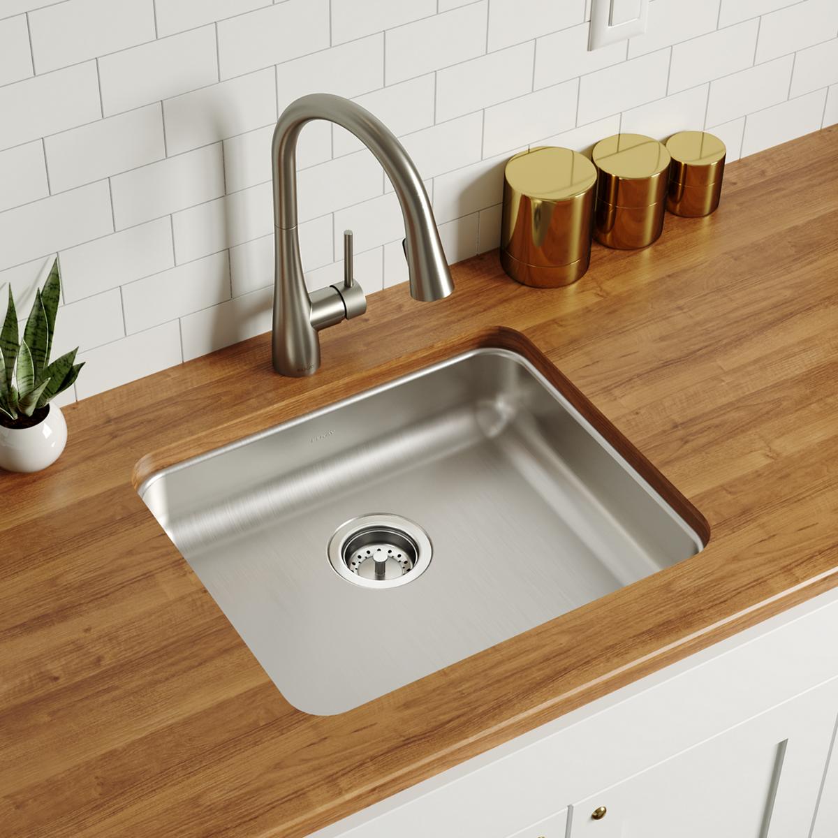 Stainless steel single bowl undermount sink installed in wood countertop with arc faucet and strainer.
