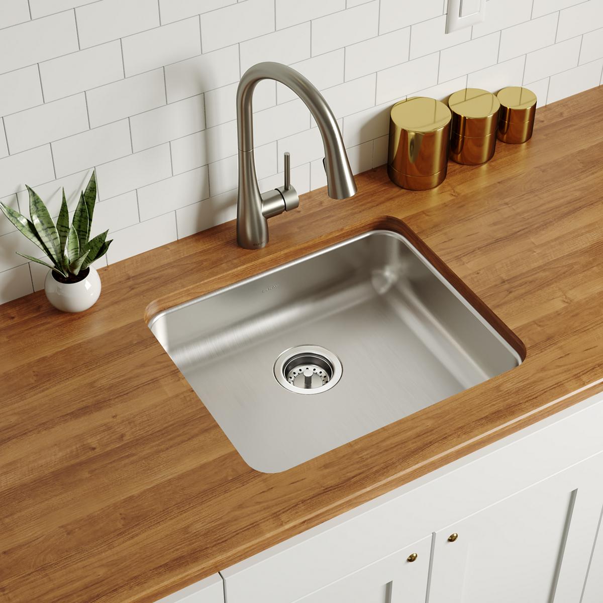 Stainless steel single bowl undermount sink with drain strainer installed in wood countertop, paired with arched faucet.
