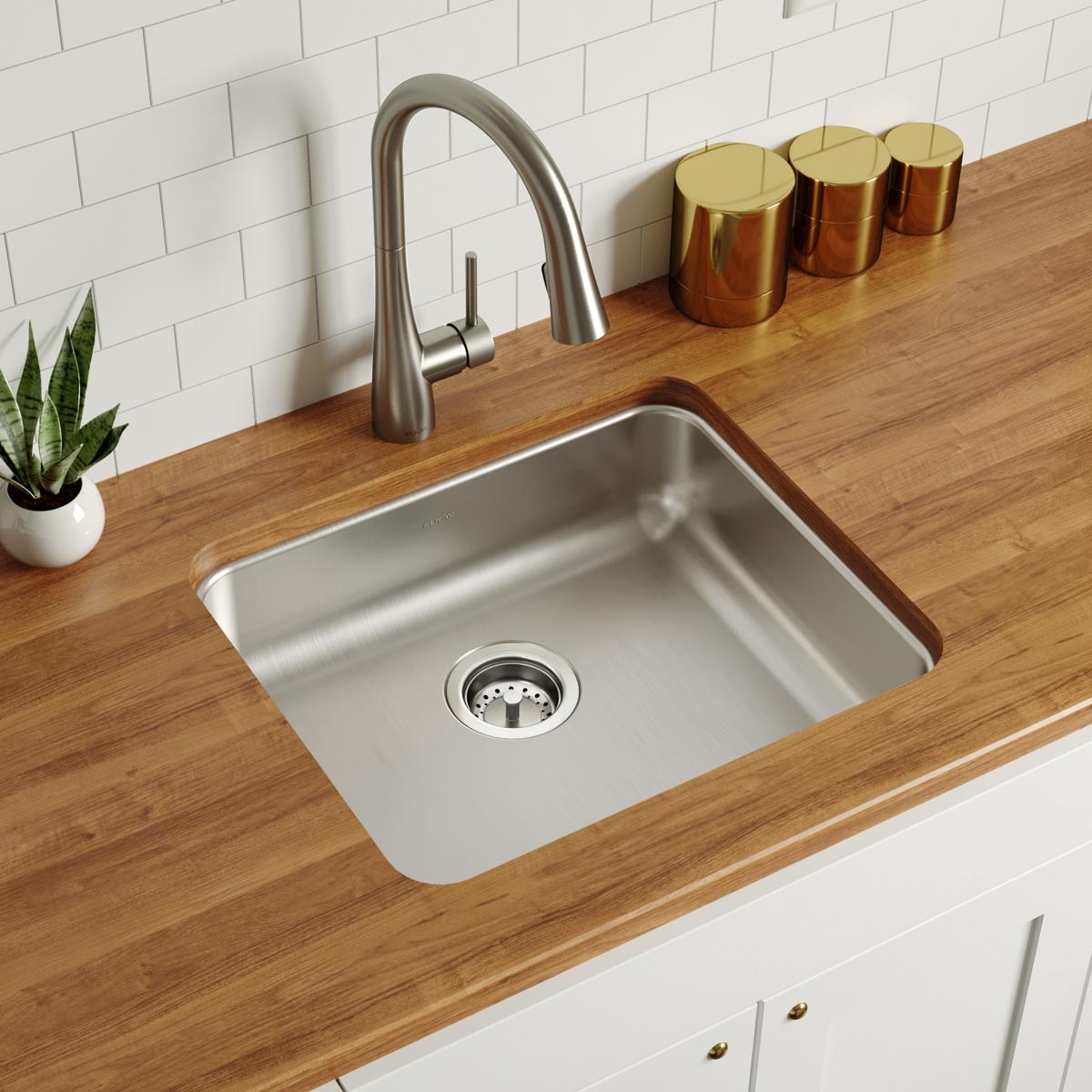 Stainless steel undermount sink with single bowl and drain strainer, installed in wooden countertop with arched faucet.