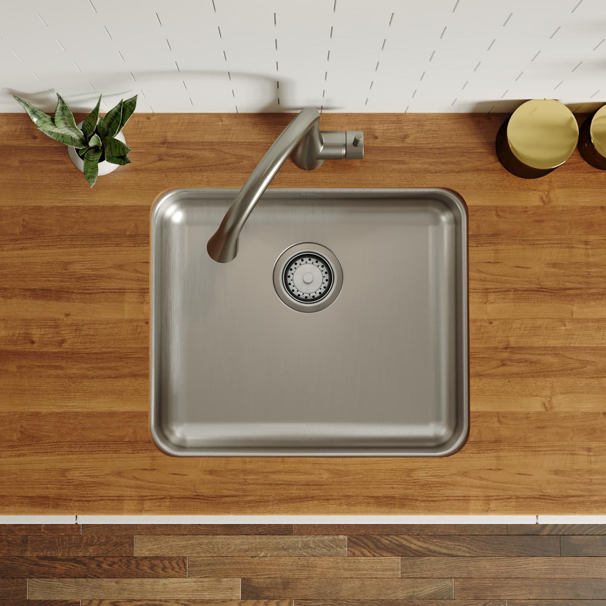 Stainless steel single bowl undermount sink with rounded corners and drain strainer, installed beneath wooden countertop.