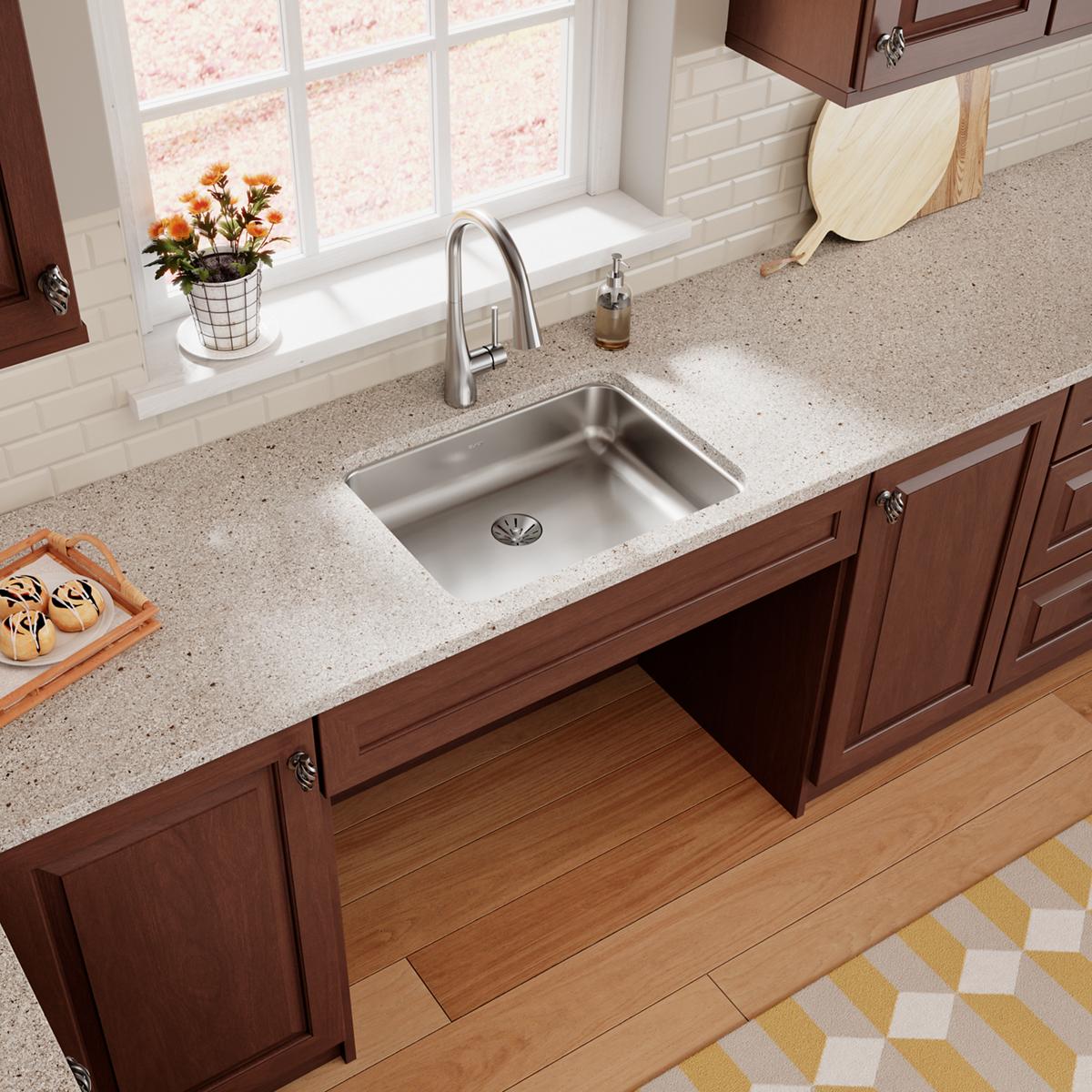Stainless steel single bowl undermount sink installed in speckled countertop with chrome faucet and drain.