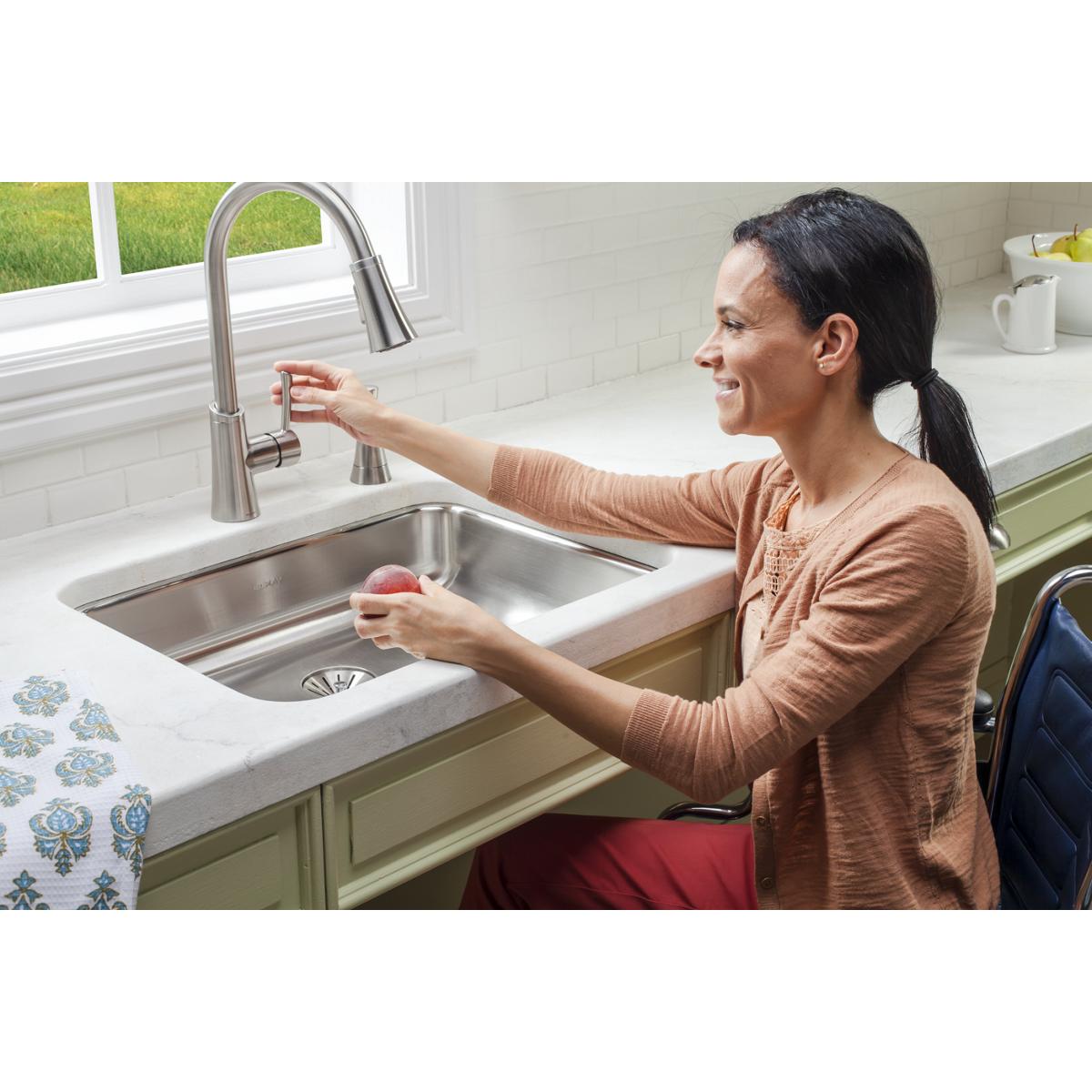 Stainless steel undermount sink with single bowl installed in white countertop, shown with pull-down faucet in kitchen.