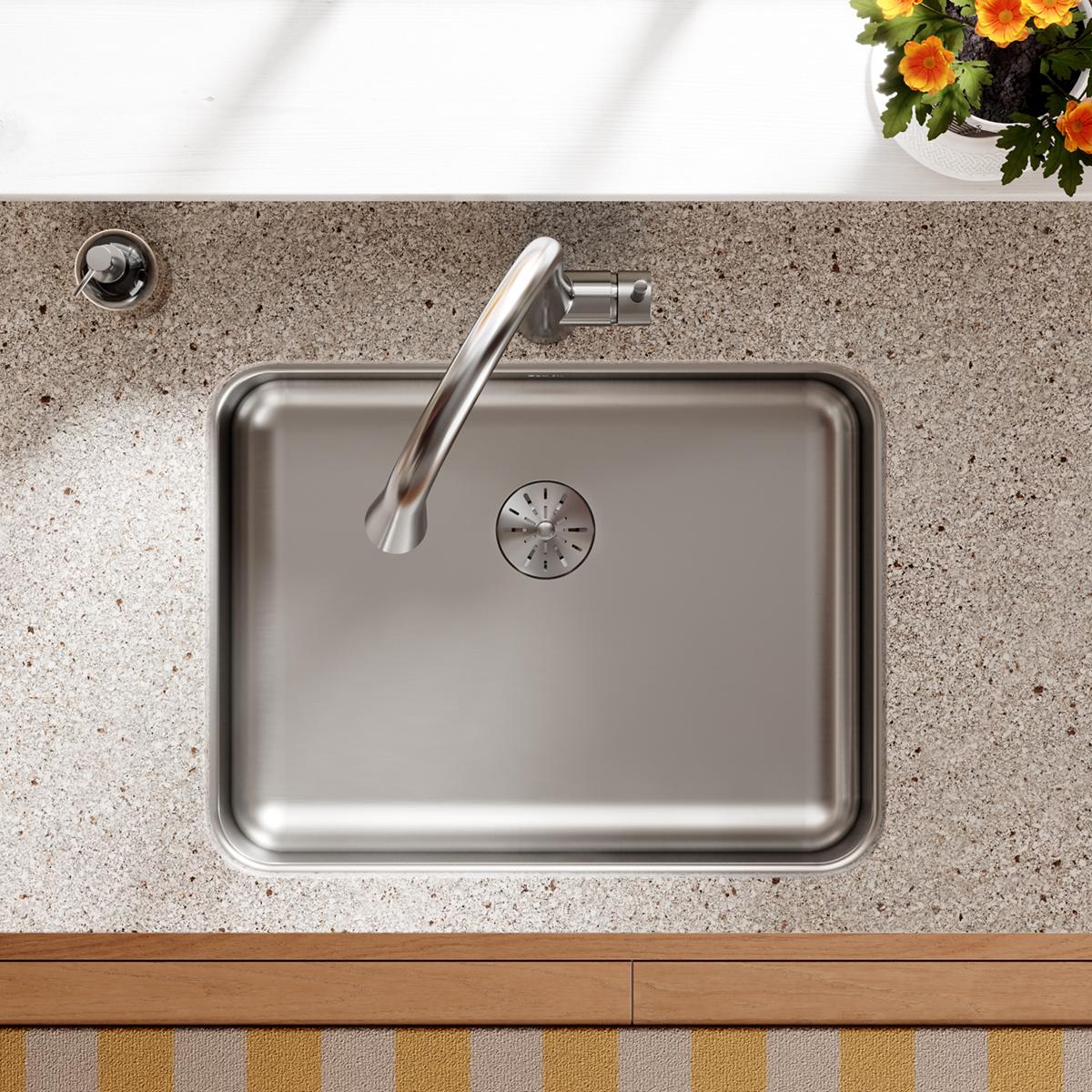 Stainless steel single bowl undermount sink with rounded corners and drain installed in speckled gray countertop.