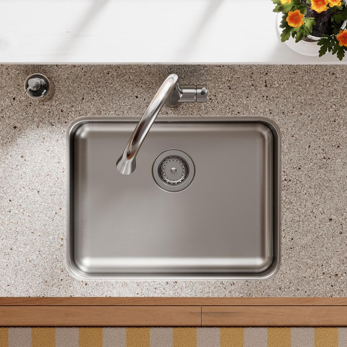 Stainless steel single bowl undermount sink installed in concrete countertop with faucet and drain visible.