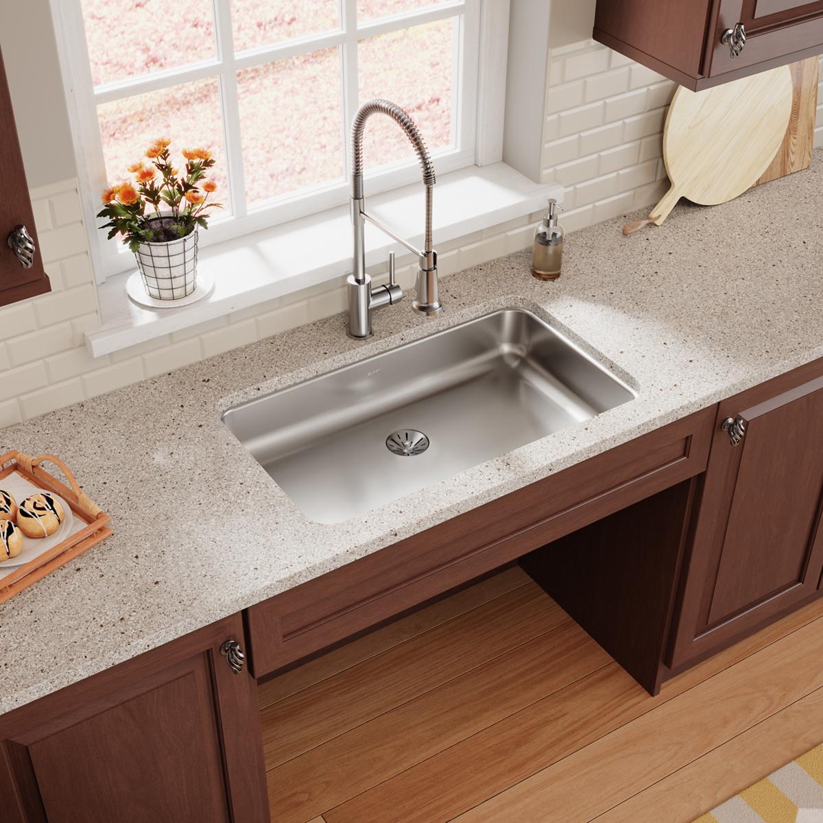 Stainless steel single bowl undermount kitchen sink installed in light countertop with chrome faucet.