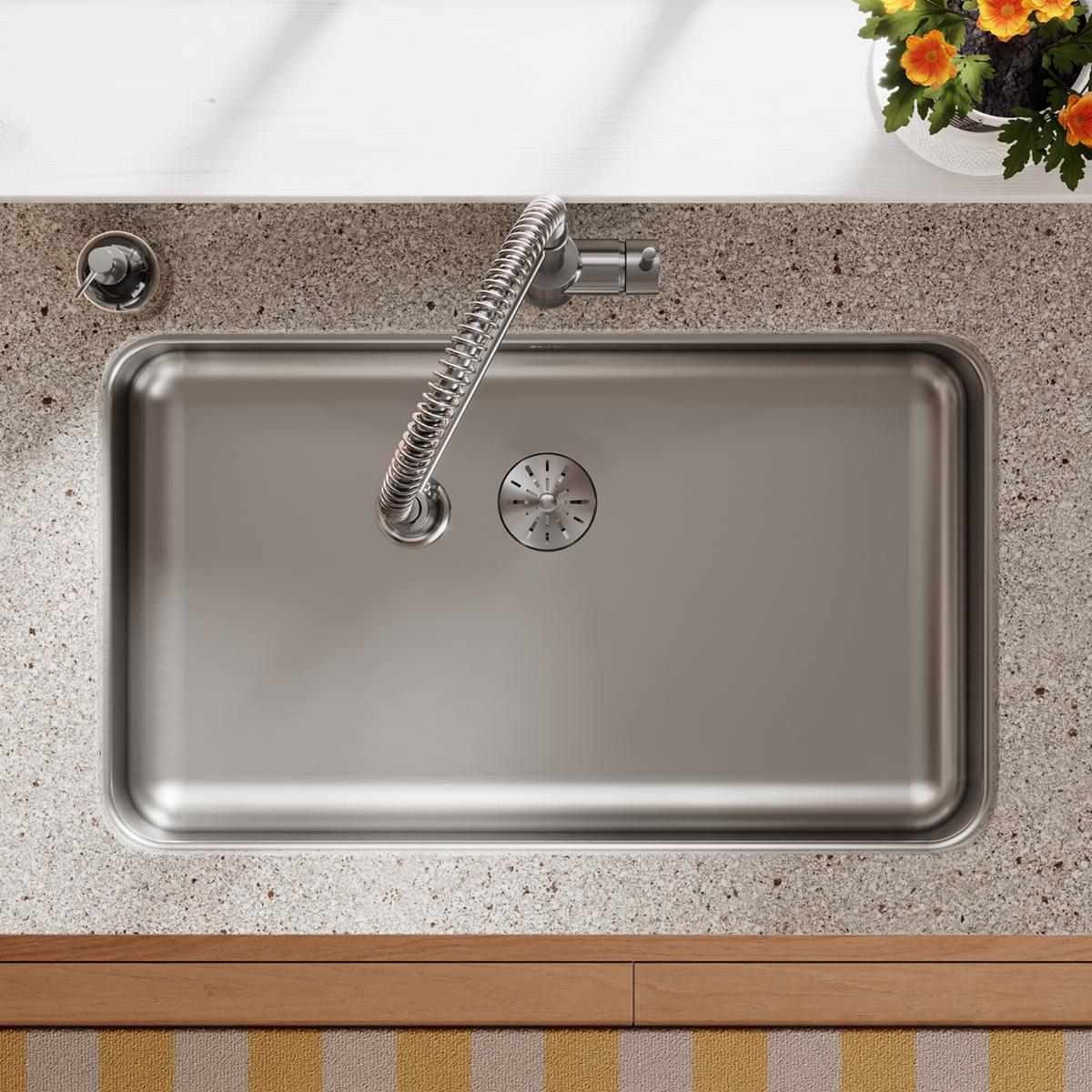 Stainless steel single bowl undermount sink installed in speckled countertop with sprayer and drain visible.