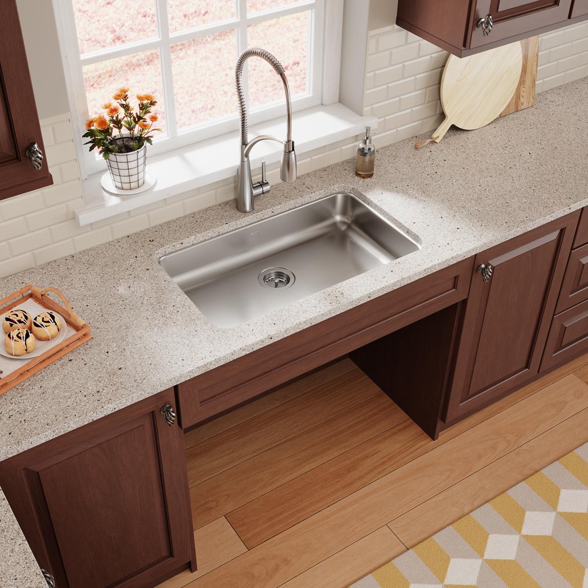 Stainless steel single bowl undermount sink installed in quartz countertop with pull-down faucet and dark wood cabinetry.