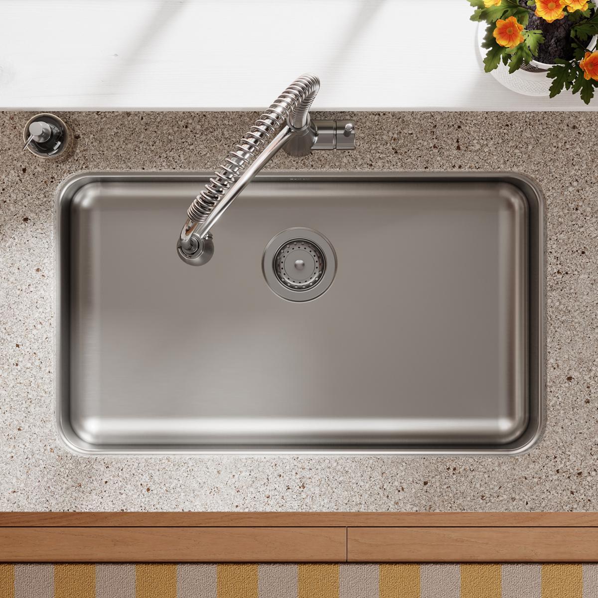 Stainless steel rectangular undermount sink with single bowl, drain, and coiled spray faucet installed in gray speckled count