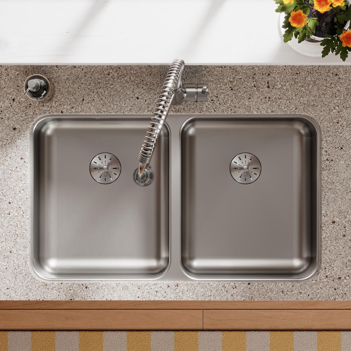 Stainless steel double bowl undermount sink with drain holes and flexible spray hose mounted beneath concrete countertop.