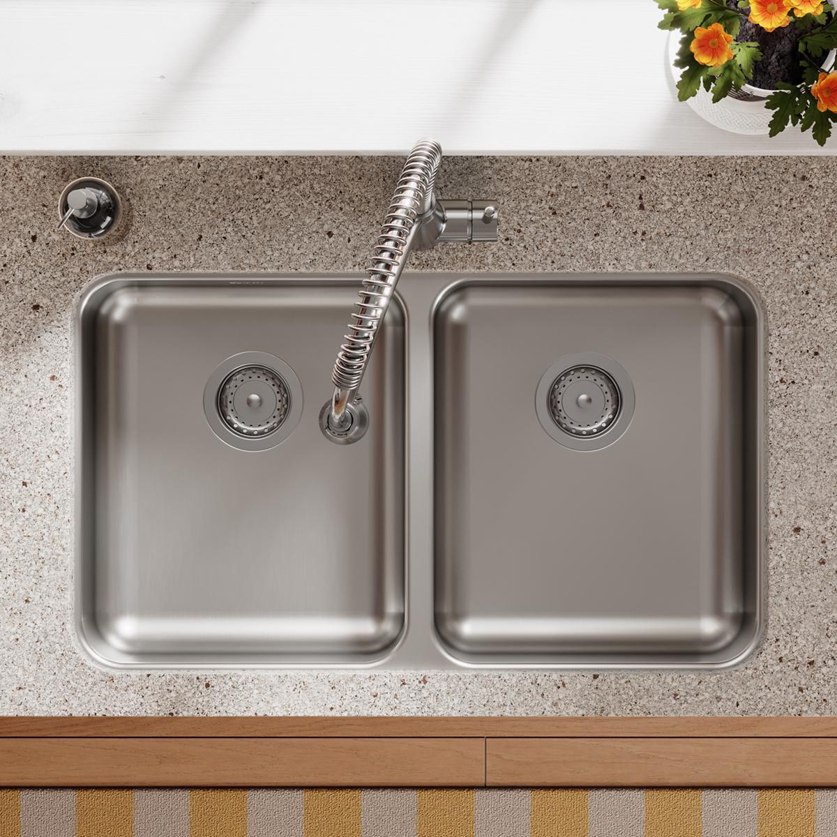 Stainless steel double bowl sink with two equal compartments, drain strainers, and coiled spray hose mounted in gray countert