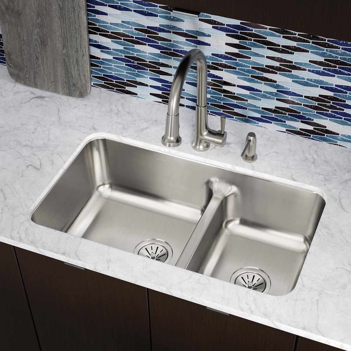 Stainless steel double bowl undermount sink with divider, brushed nickel faucet, and drain strainers installed in marble coun