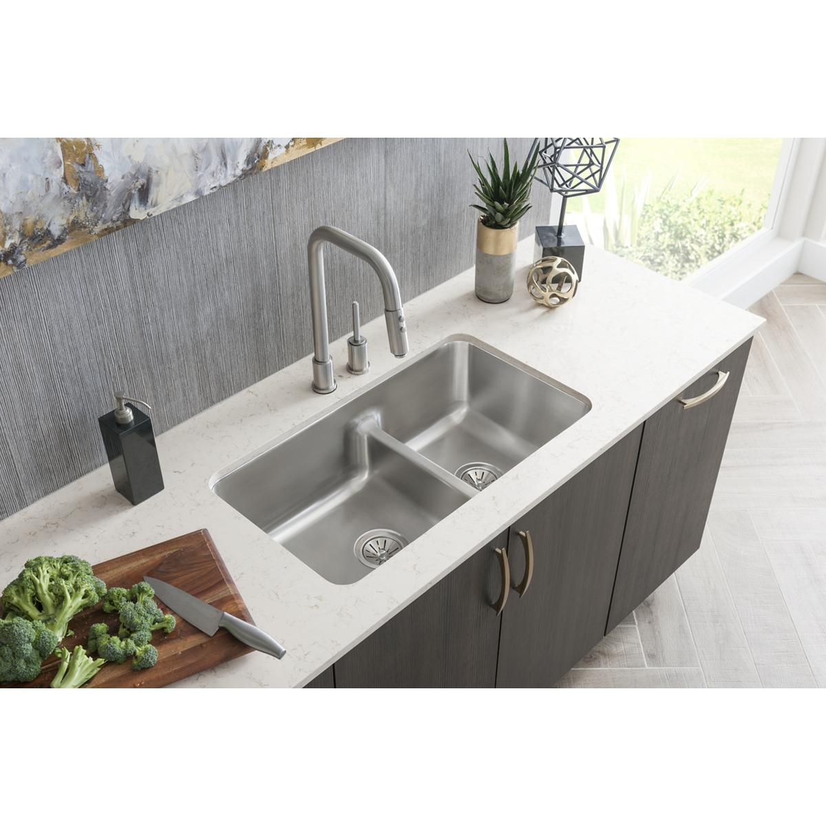 Stainless steel double bowl undermount sink with divider installed in white countertop next to faucet.