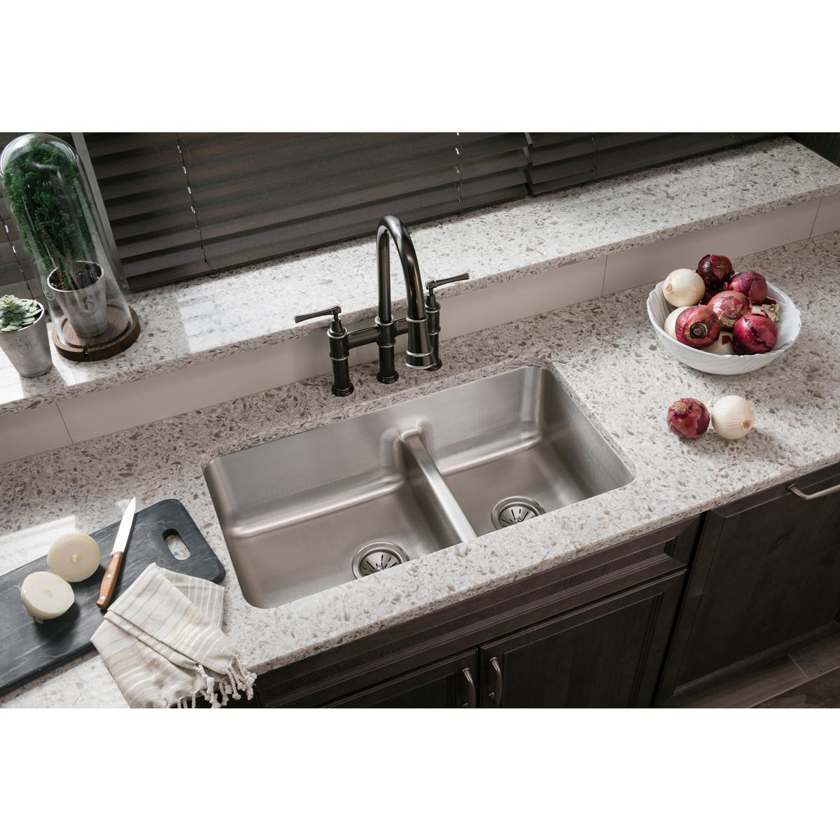 Stainless steel double bowl undermount sink installed in granite countertop with black faucet and divide between bowls.