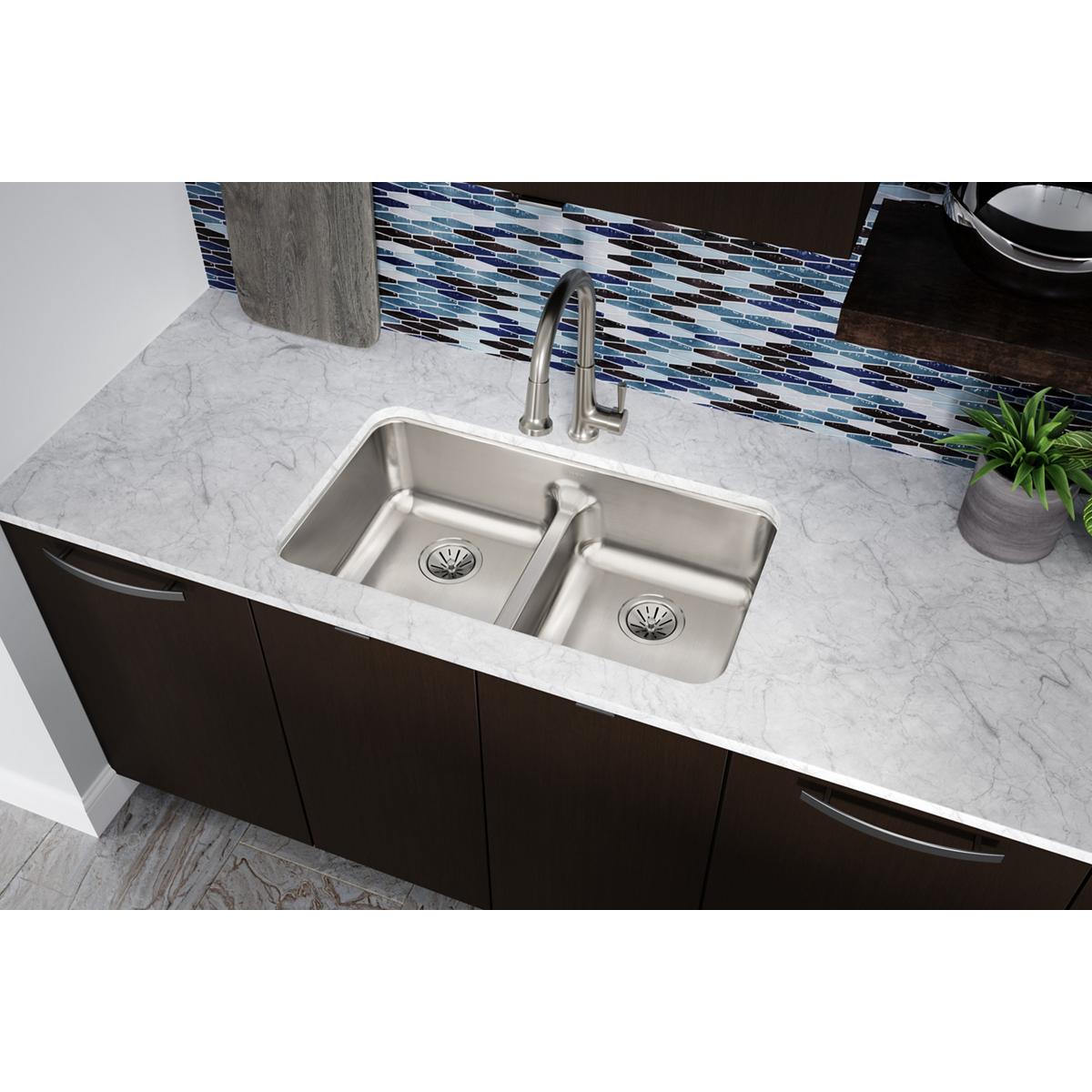Stainless steel double bowl undermount sink with center divider installed in marble countertop with faucet.