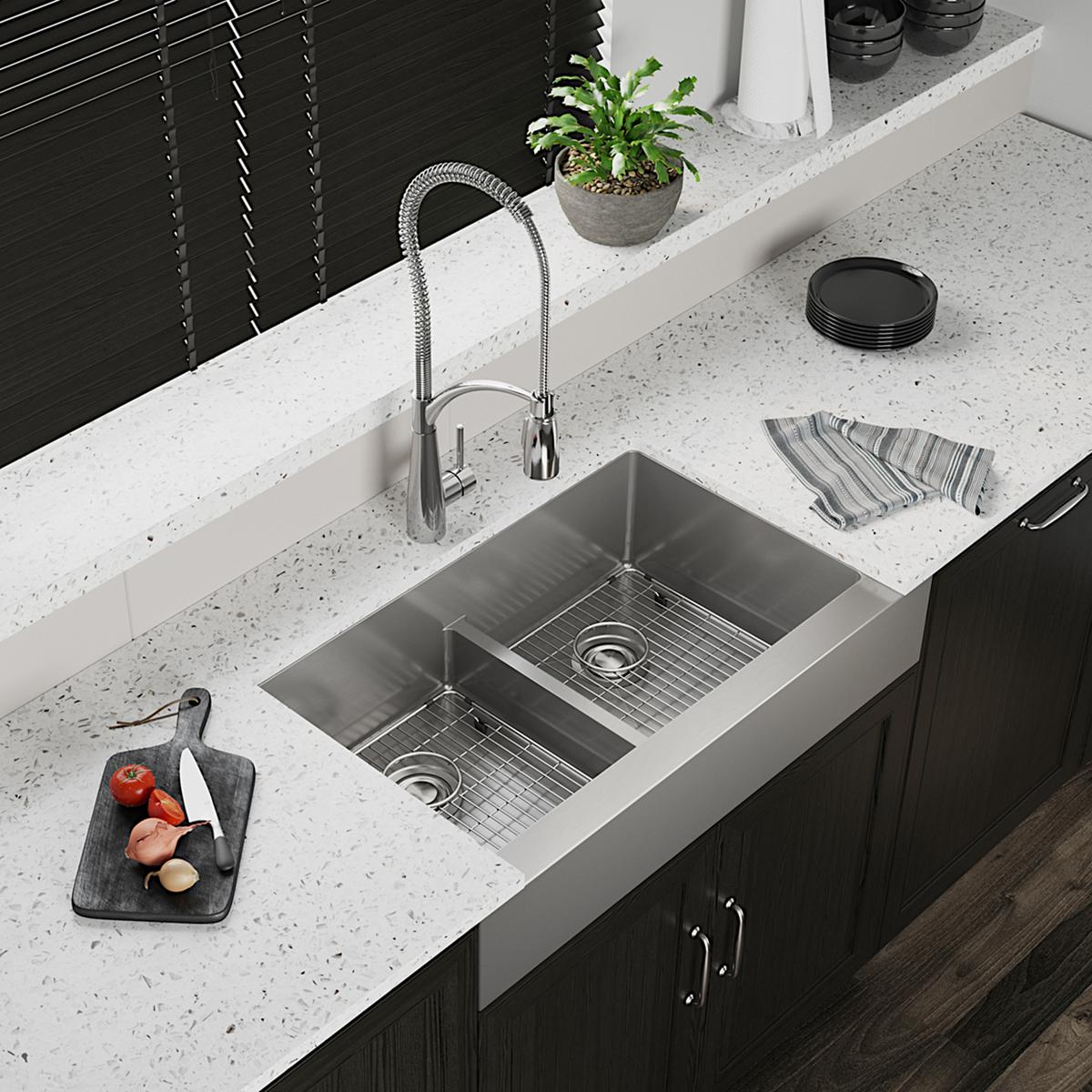 Stainless steel double bowl farmhouse sink with divider, grid inserts, and pull-down faucet installed in white countertop.