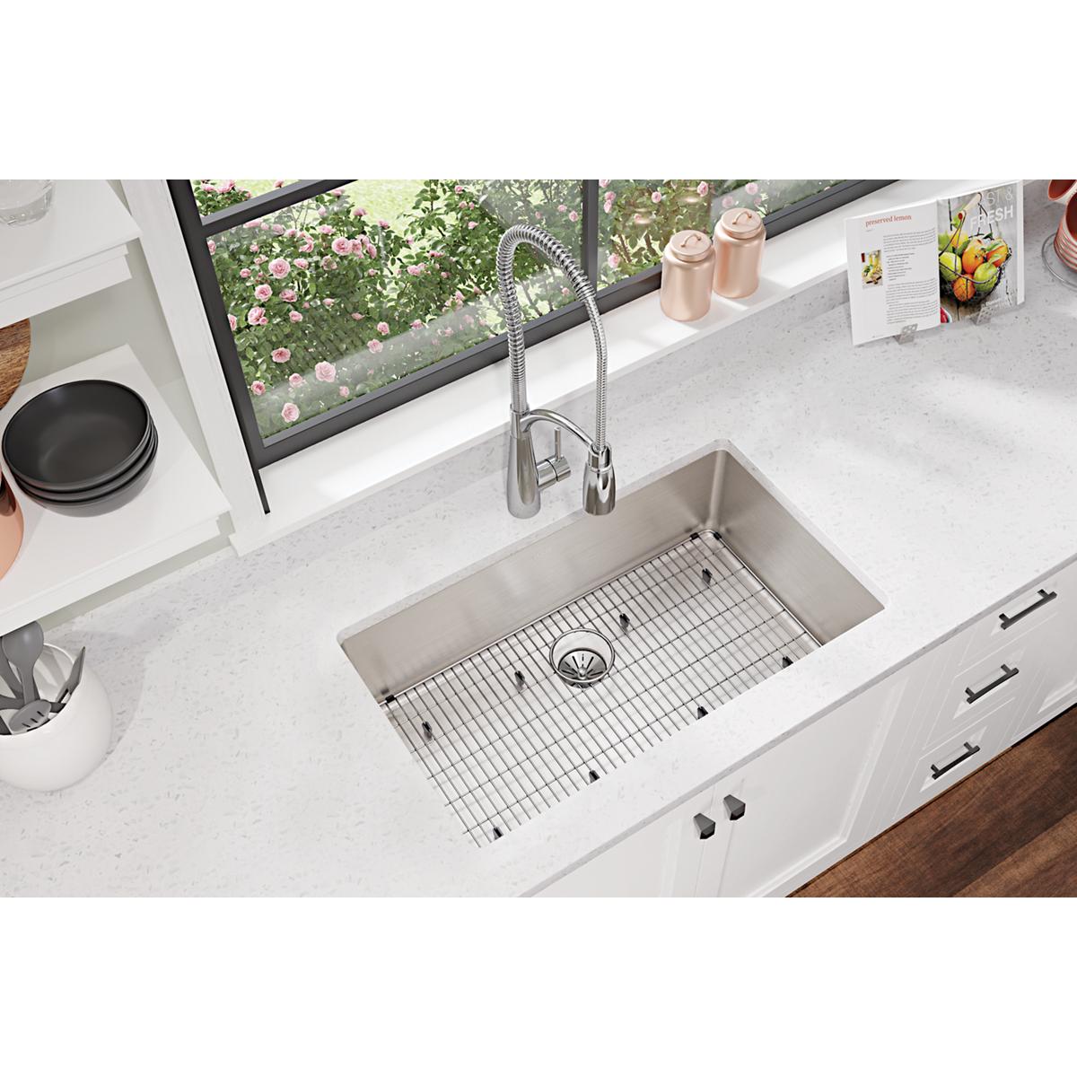 Stainless steel sink grid with wire pattern, positioned in undermount kitchen sink basin.