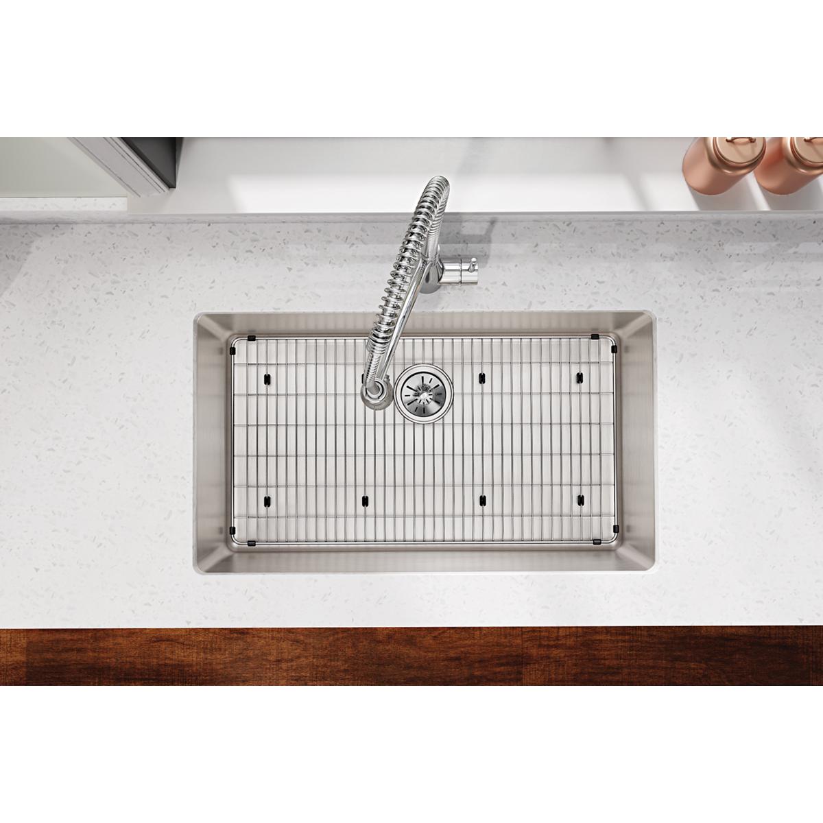 Stainless steel sink bottom grid with vertical bars and mounting feet, installed in undermount sink basin.