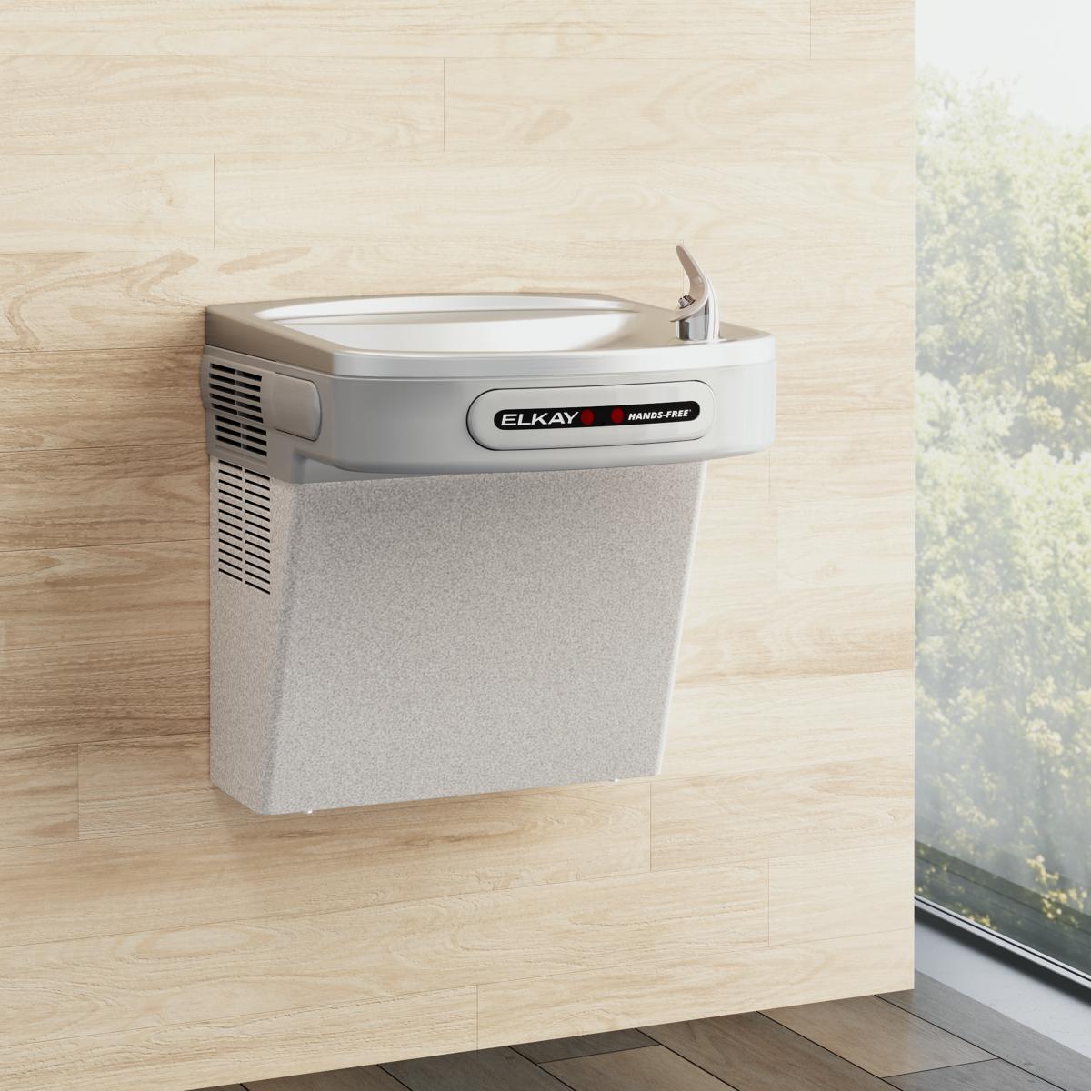 Light gray granite wall-mounted water cooler with white basin and hands-free activation lever mounted on light wood wall.