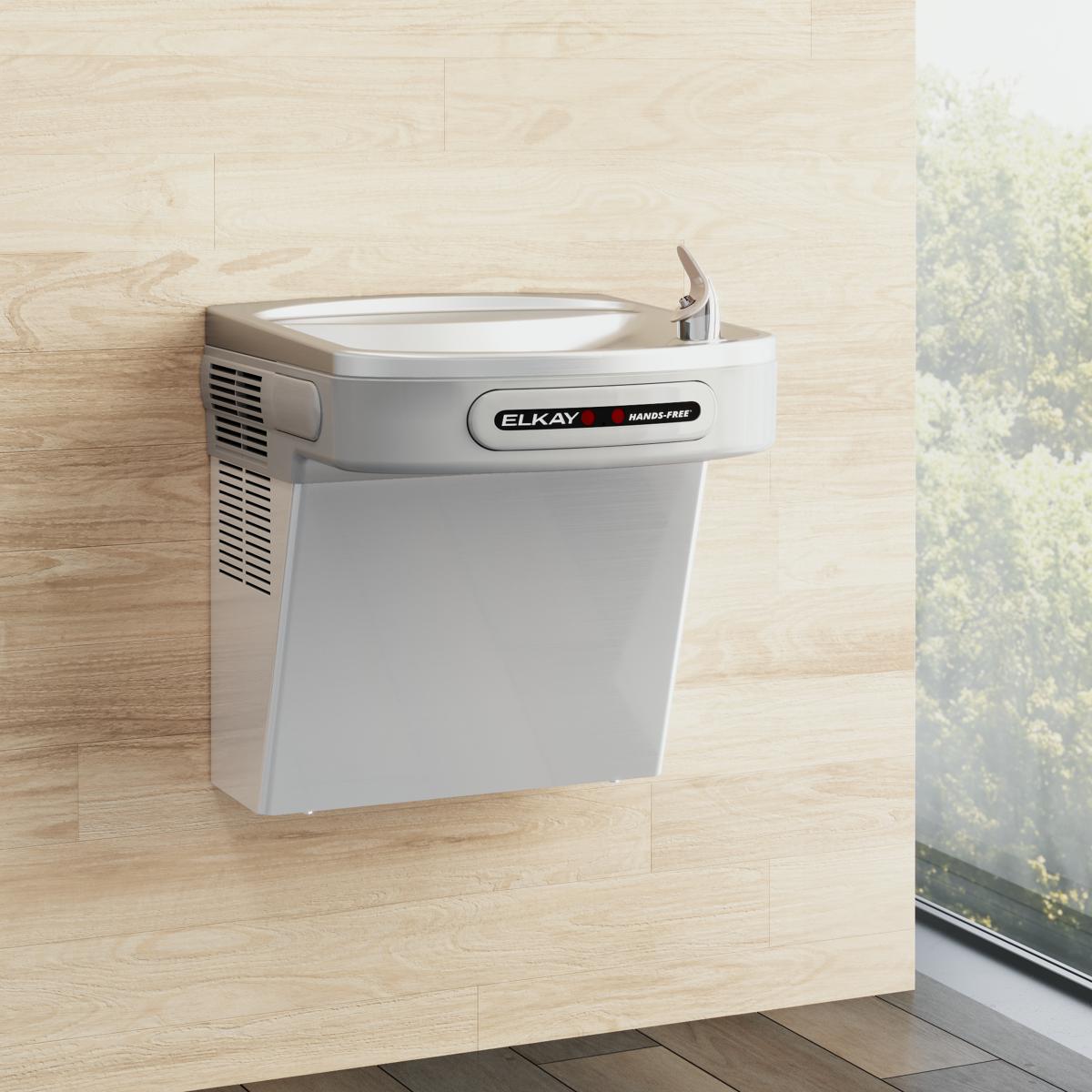 White Elkay wall-mounted water cooler with hands-free activation and stainless steel basin mounted on light wood wall.