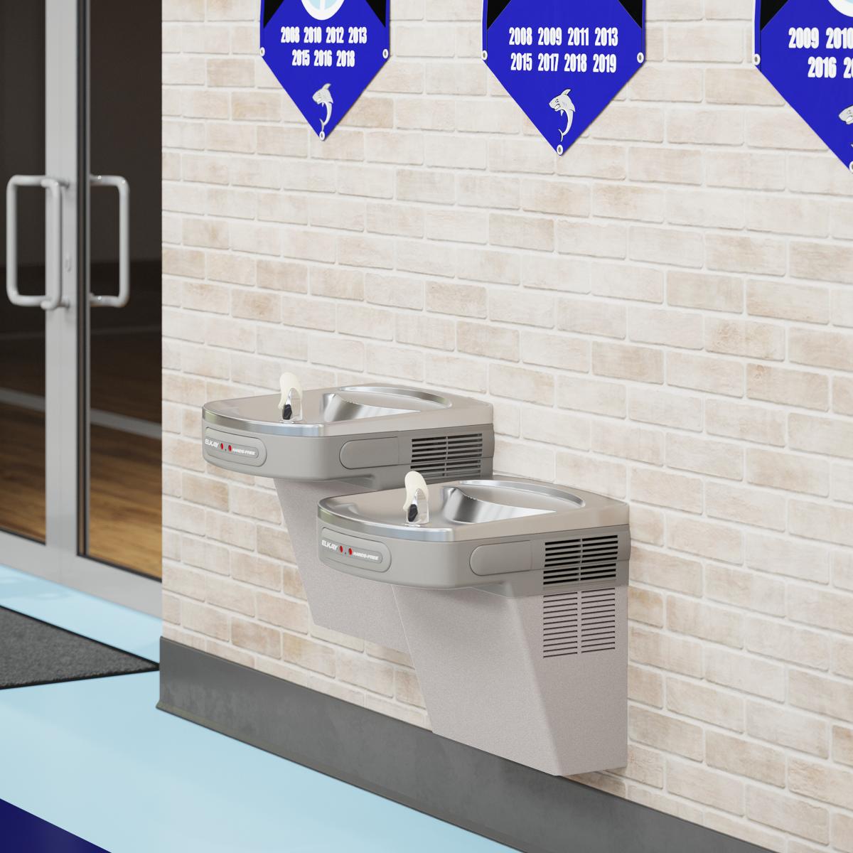 Light gray dual water cooler with two stainless steel basins mounted on brick wall at different heights.