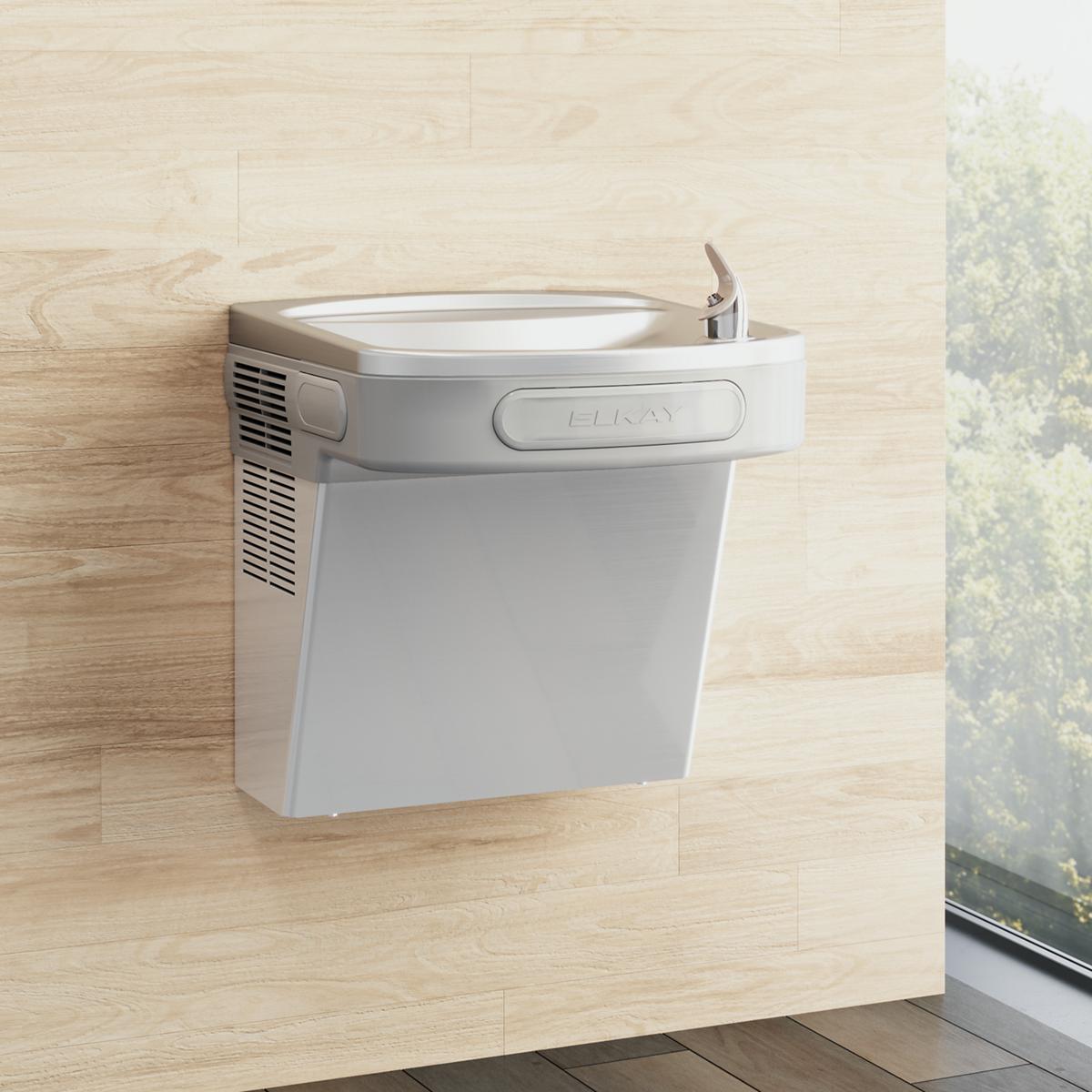 White Elkay wall-mounted water cooler with integral drinking fountain bowl and stainless steel spout mounted on wooden wall.