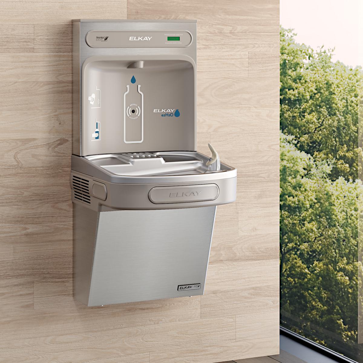 Stainless steel wall-mounted water cooler with bottle filling station and drinking fountain mounted on light wood wall.