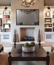 Black-framed television mounted on wall above fireplace in living room with built-in shelving on either side.