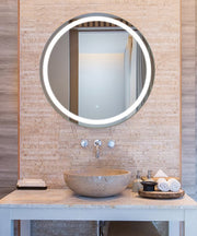Round lighted mirror with LED halo frame mounted above bathroom vanity with stone vessel sink.