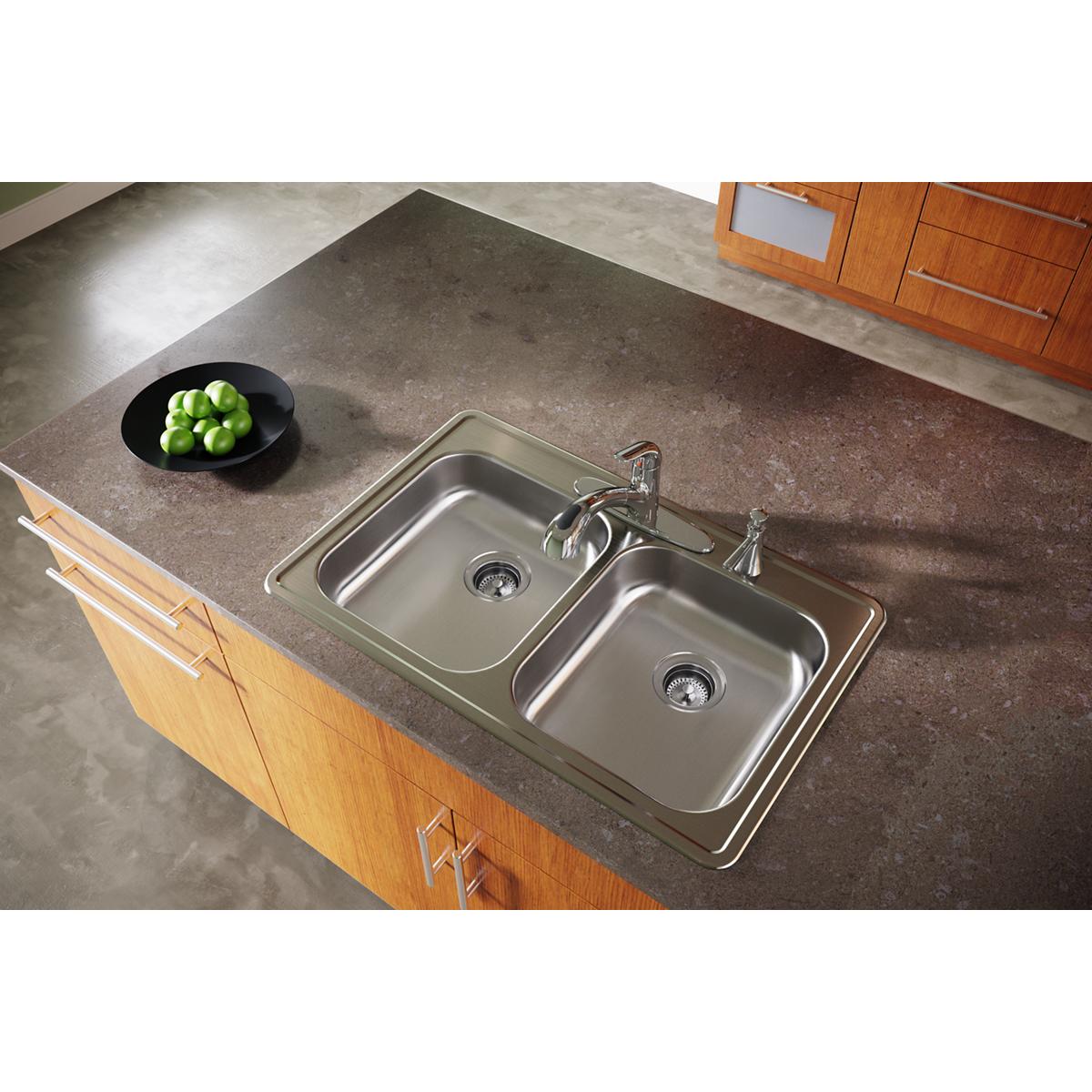 Stainless steel double bowl drop-in sink with two faucet holes installed in dark countertop with wood cabinetry.