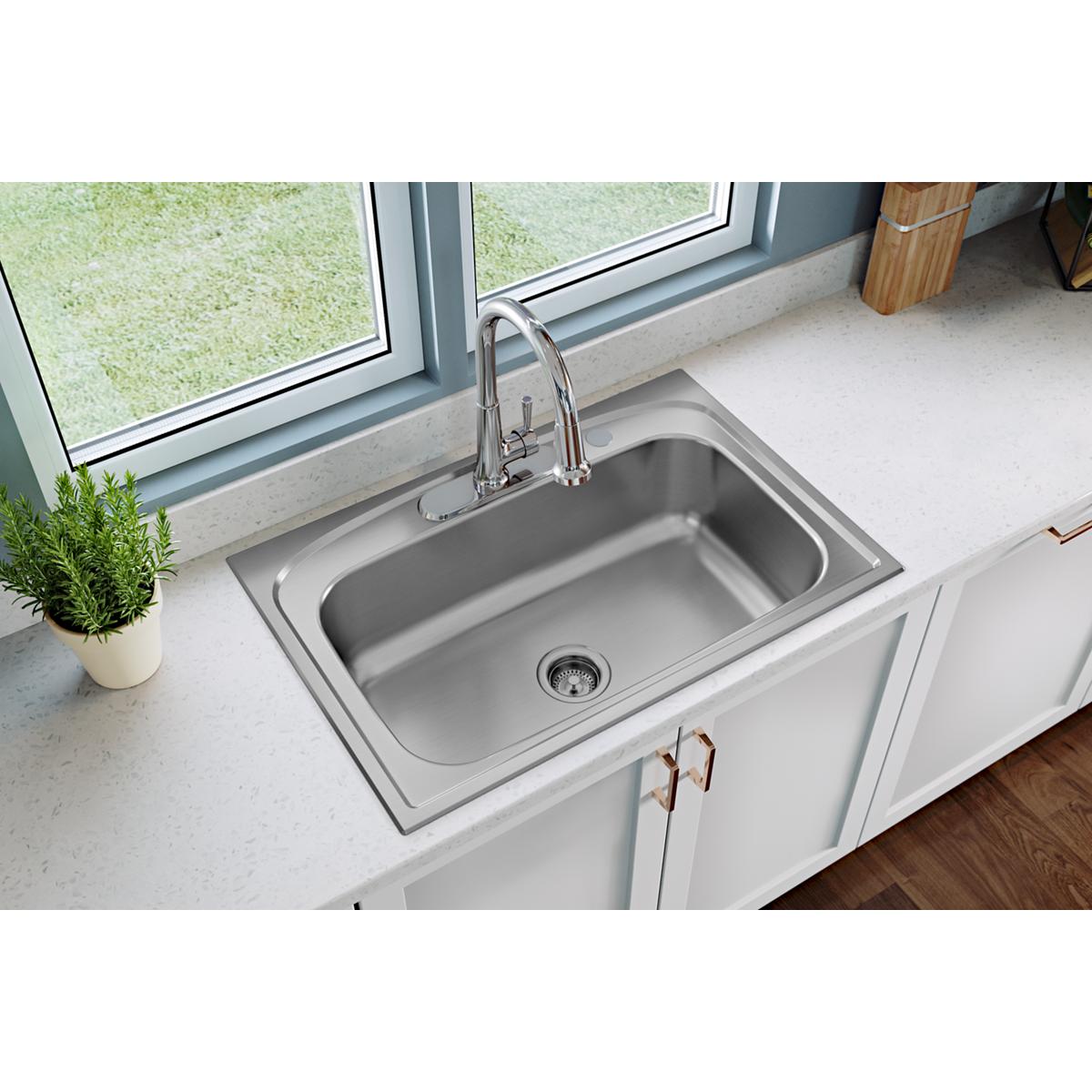 Chrome kitchen faucet with single lever handle and pull-down spray installed over stainless steel sink in white countertop.