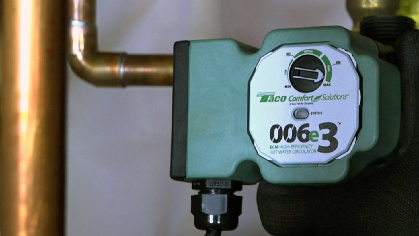 Green recirculating pump with 'Taco Comfort Solutions' branding attached to a pipe.