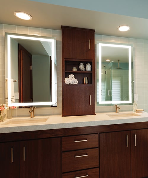 Rectangular lighted mirror with white LED border frame mounted above bathroom vanity with dark wood cabinetry.